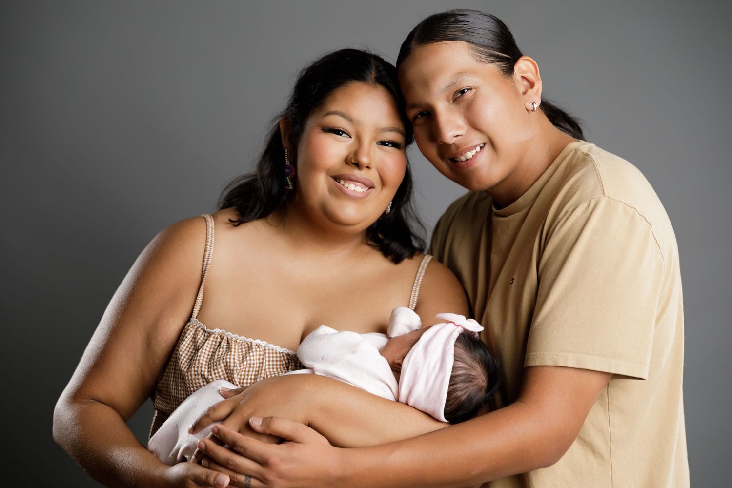 Happy couple smiling and holding their newborn baby in a professional studio portrait photo.