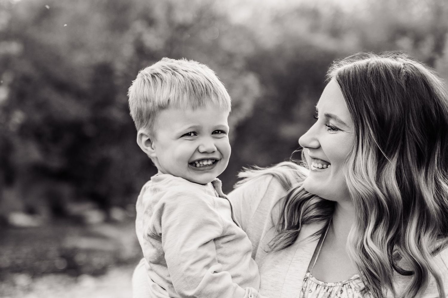 Black and white photo of a laughing toddler boy being held by a smiling young woman outdoors.