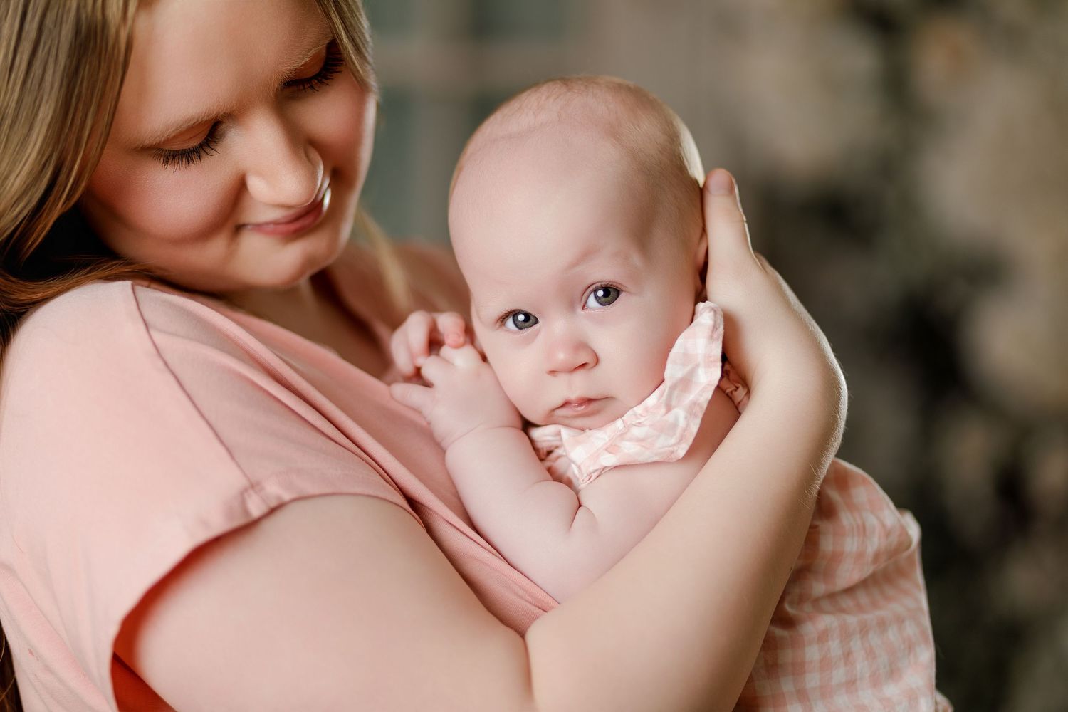Close-up of a young mother in pink gently cradling her wide-eyed infant against her chest.