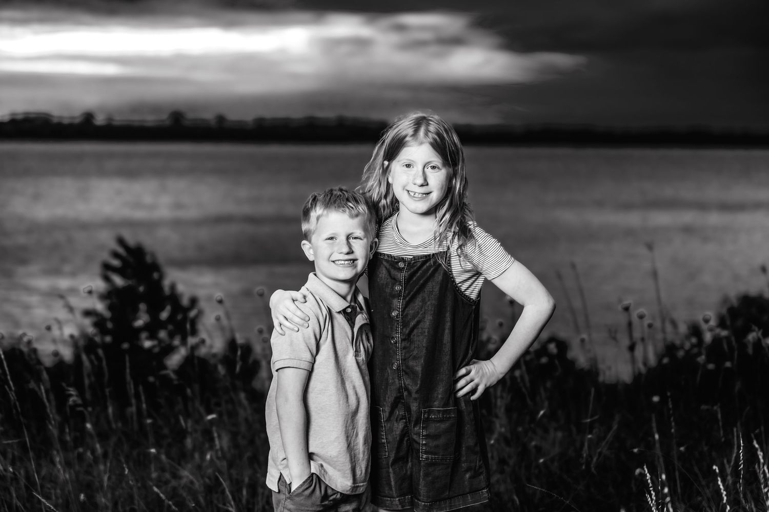 Black and white portrait of two children posing together in front of a water view.