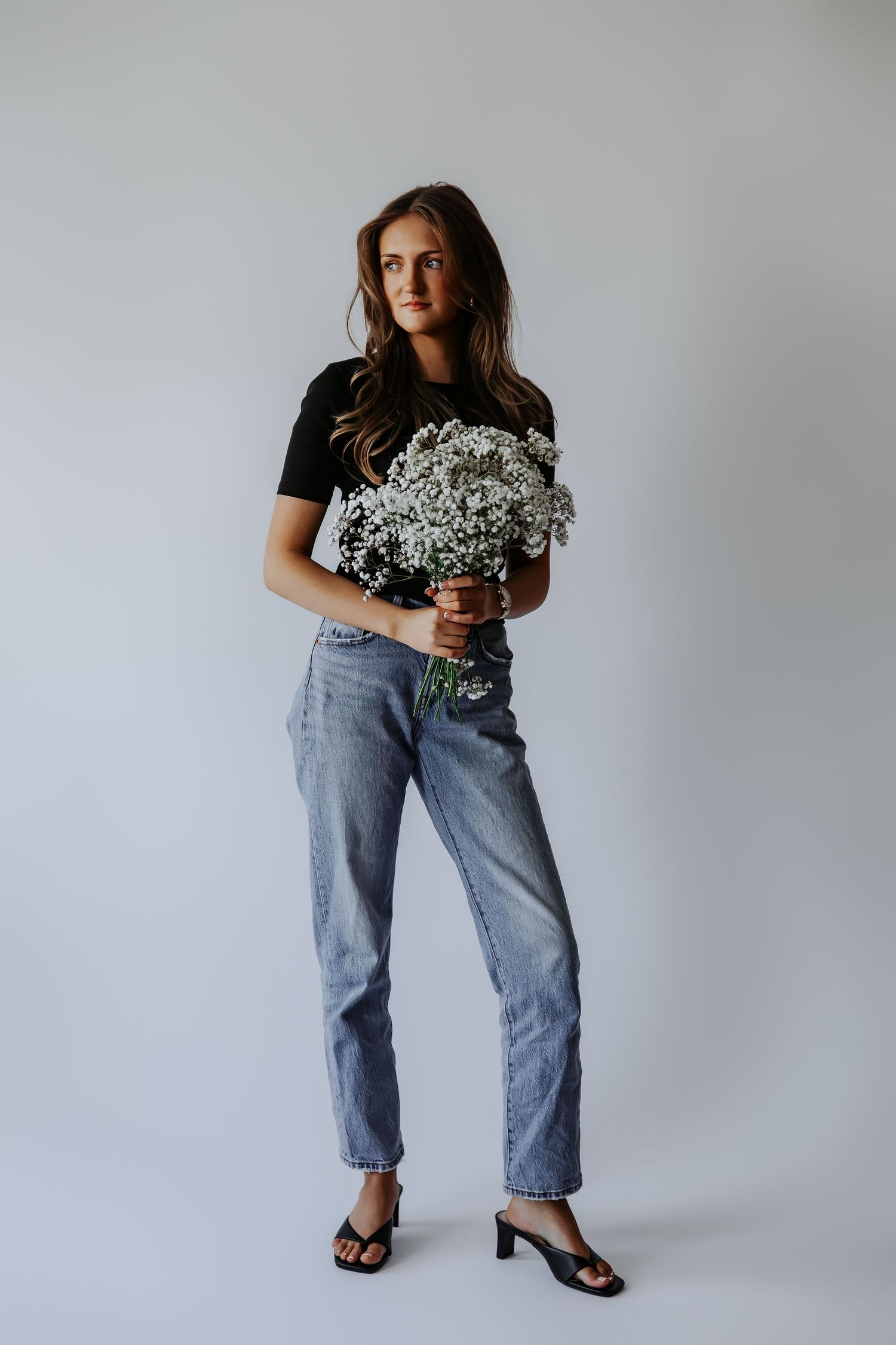 Young woman standing holding white baby's breath flowers wearing black tee and light blue jeans.