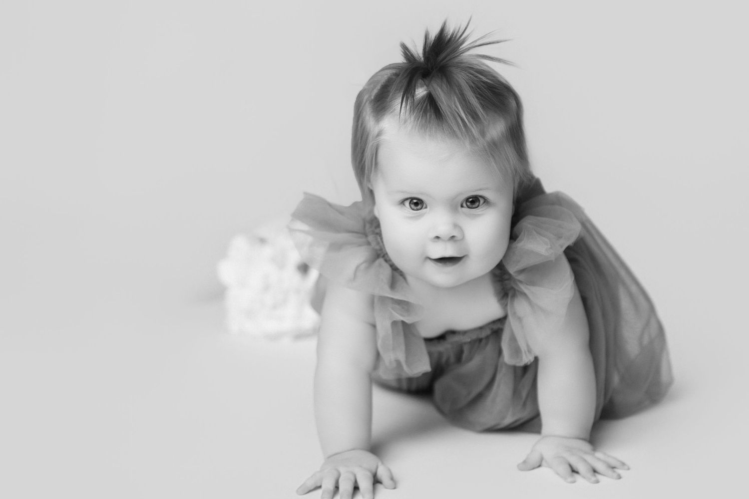 Black and white portrait of a baby in a gray outfit crawling on a white background.