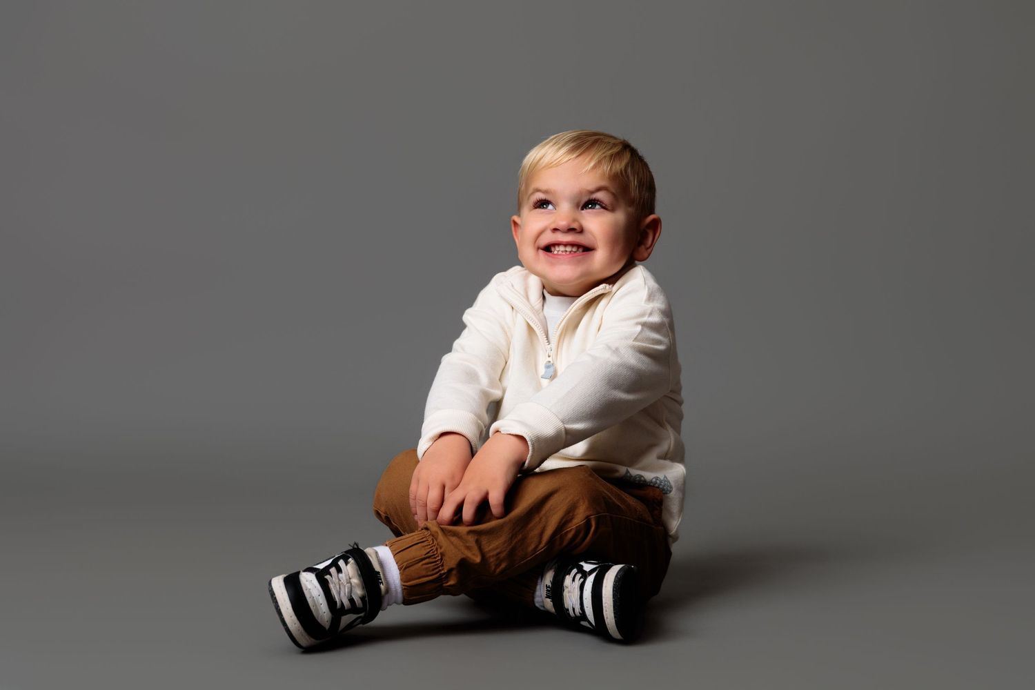 Series of photos showing toddler in white shirt and brown pants against gray backdrop.
