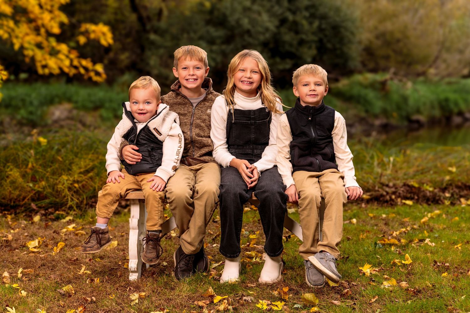 A group sitting on fallen autumn leaves wearing coordinated brown and white outfits in a natural outdoor setting.