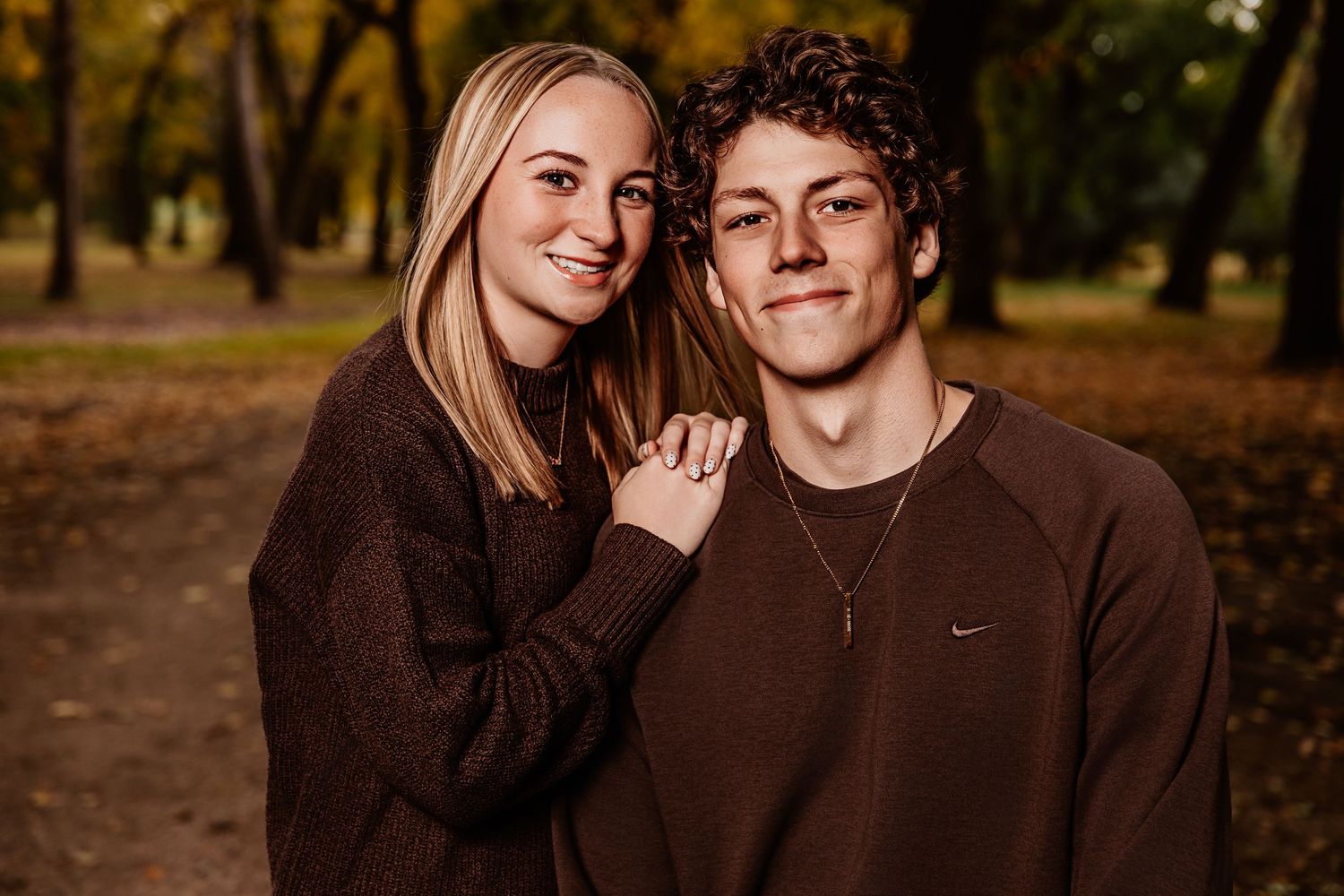A family poses together in an autumn forest setting wearing coordinated earth-tone outfits.
