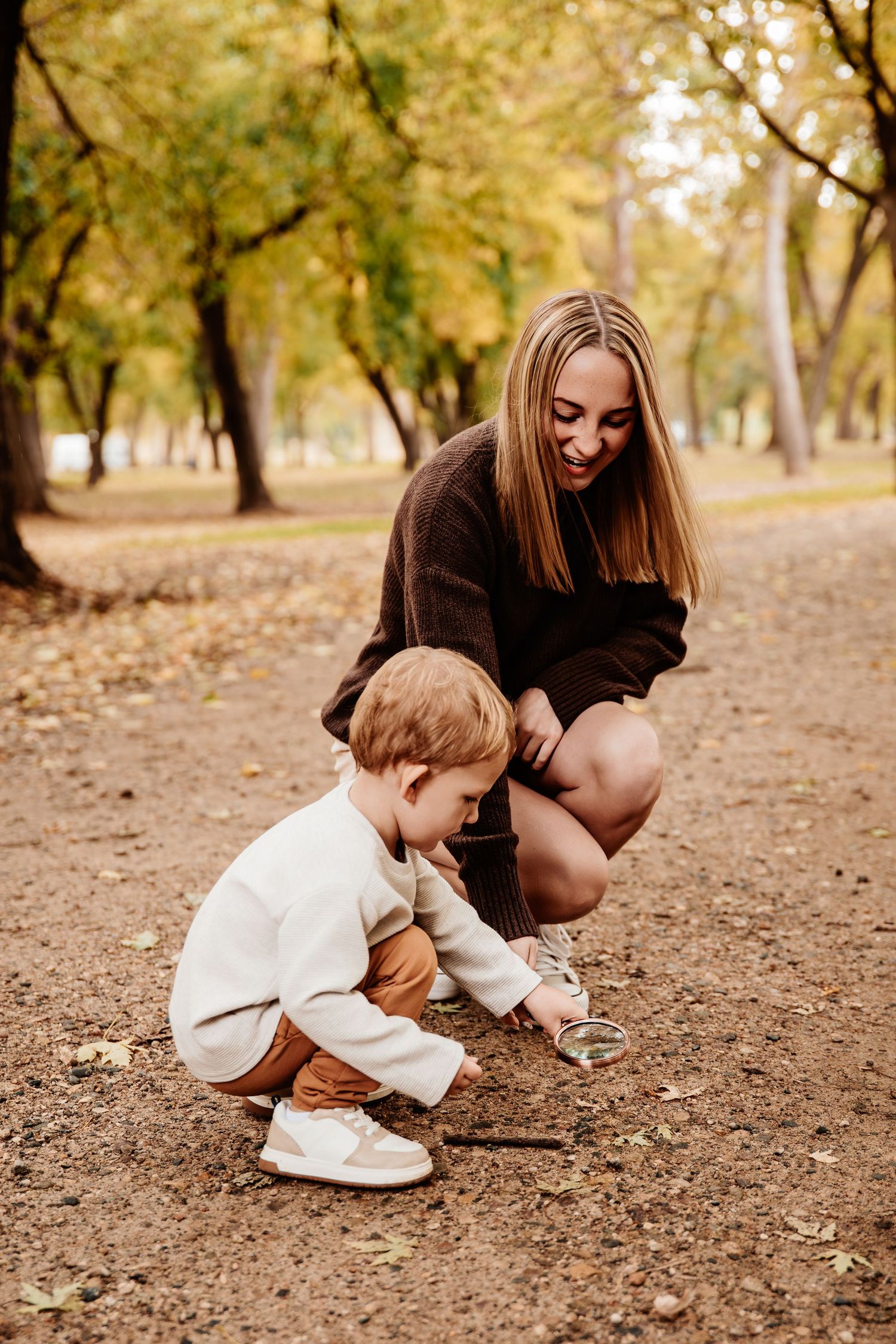 Parent and child explore nature together while crouching in a park setting.