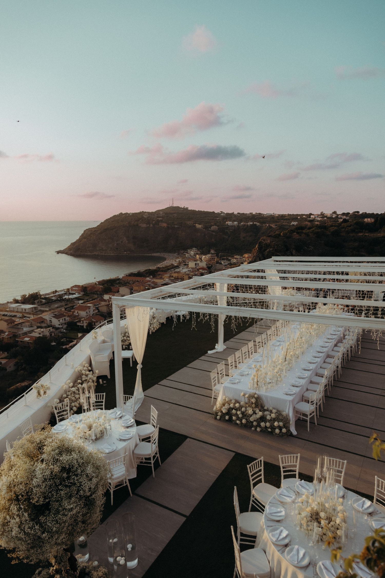 Wedding couple standing on hilltop overlooking Sicily’s vast landscape and coastline.