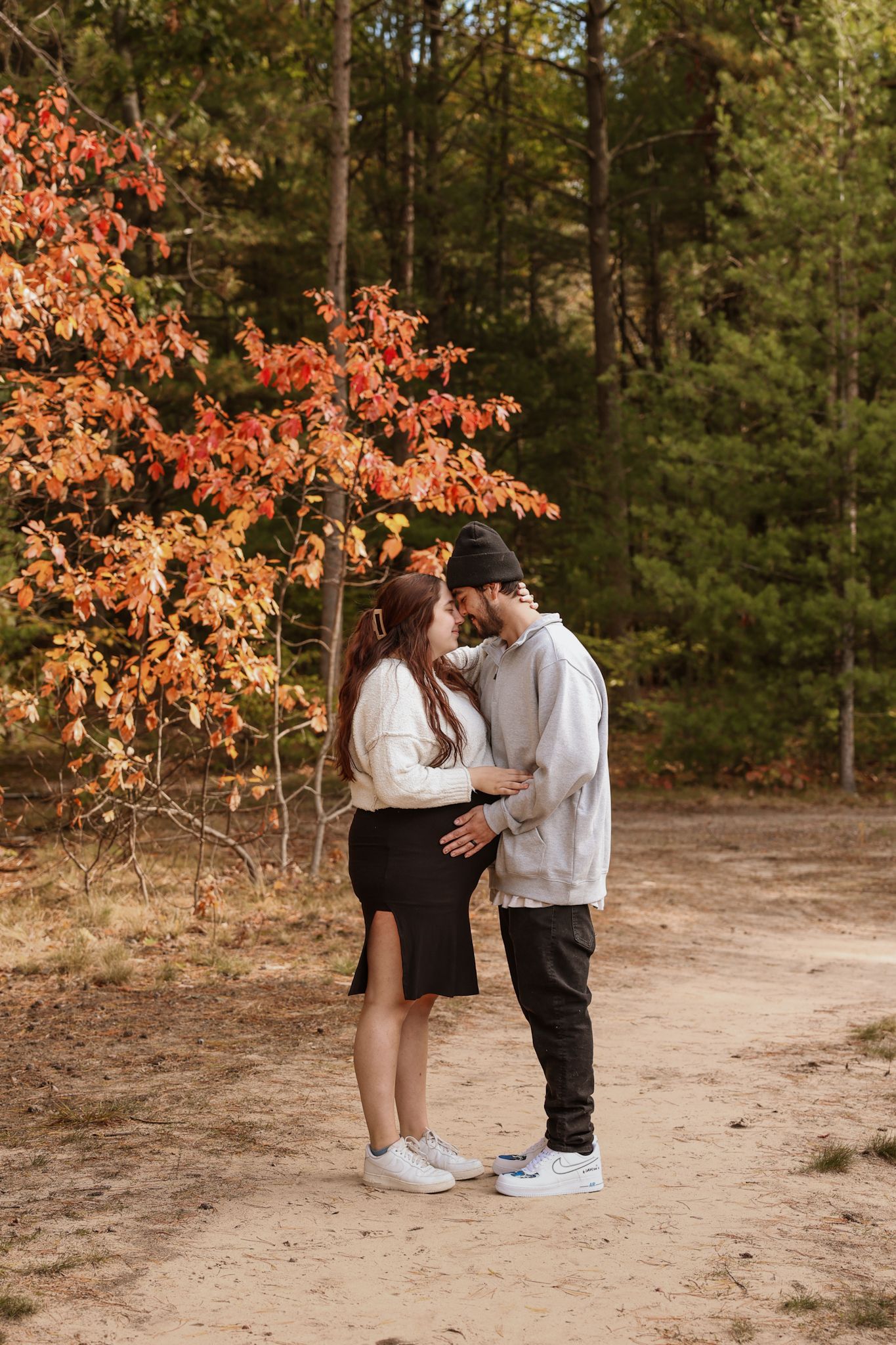 A couple shares an intimate moment beneath vibrant orange autumn foliage in a wooded setting.