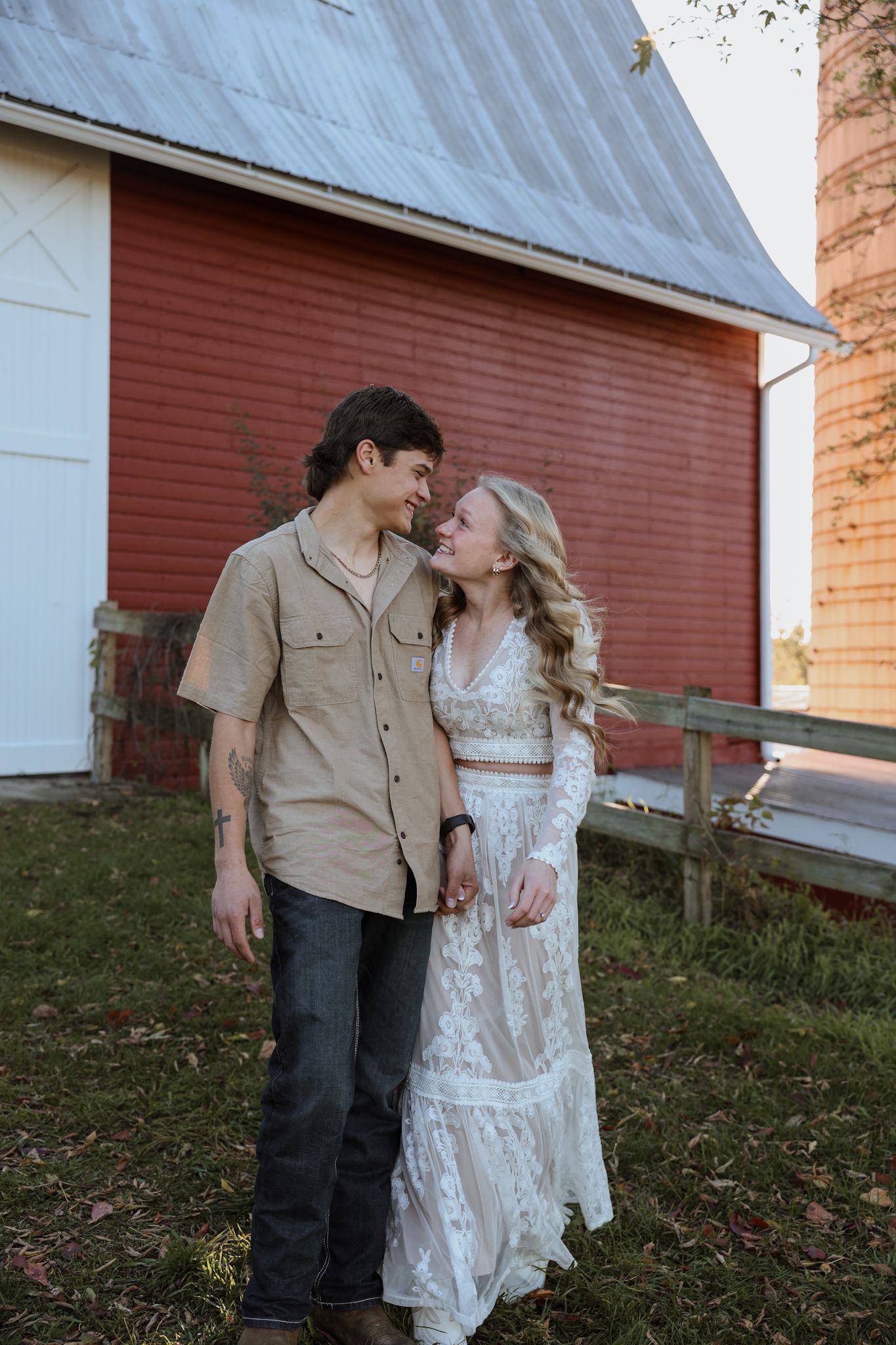 A romantic couple shares tender moments in front of a rustic red barn during a countryside engagement photo session.