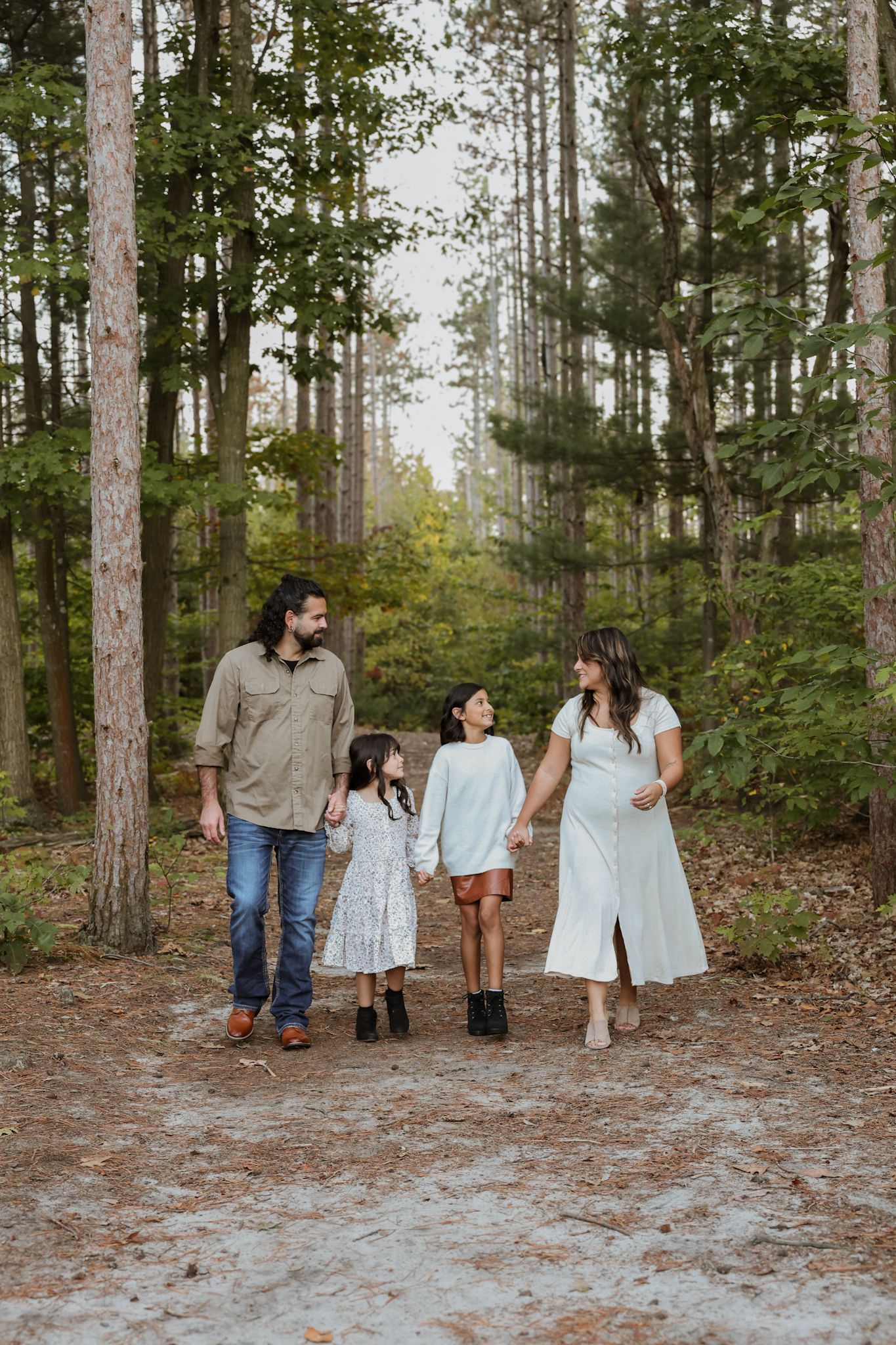 A group walks together through a serene pine forest setting wearing coordinated light-colored casual outfits.