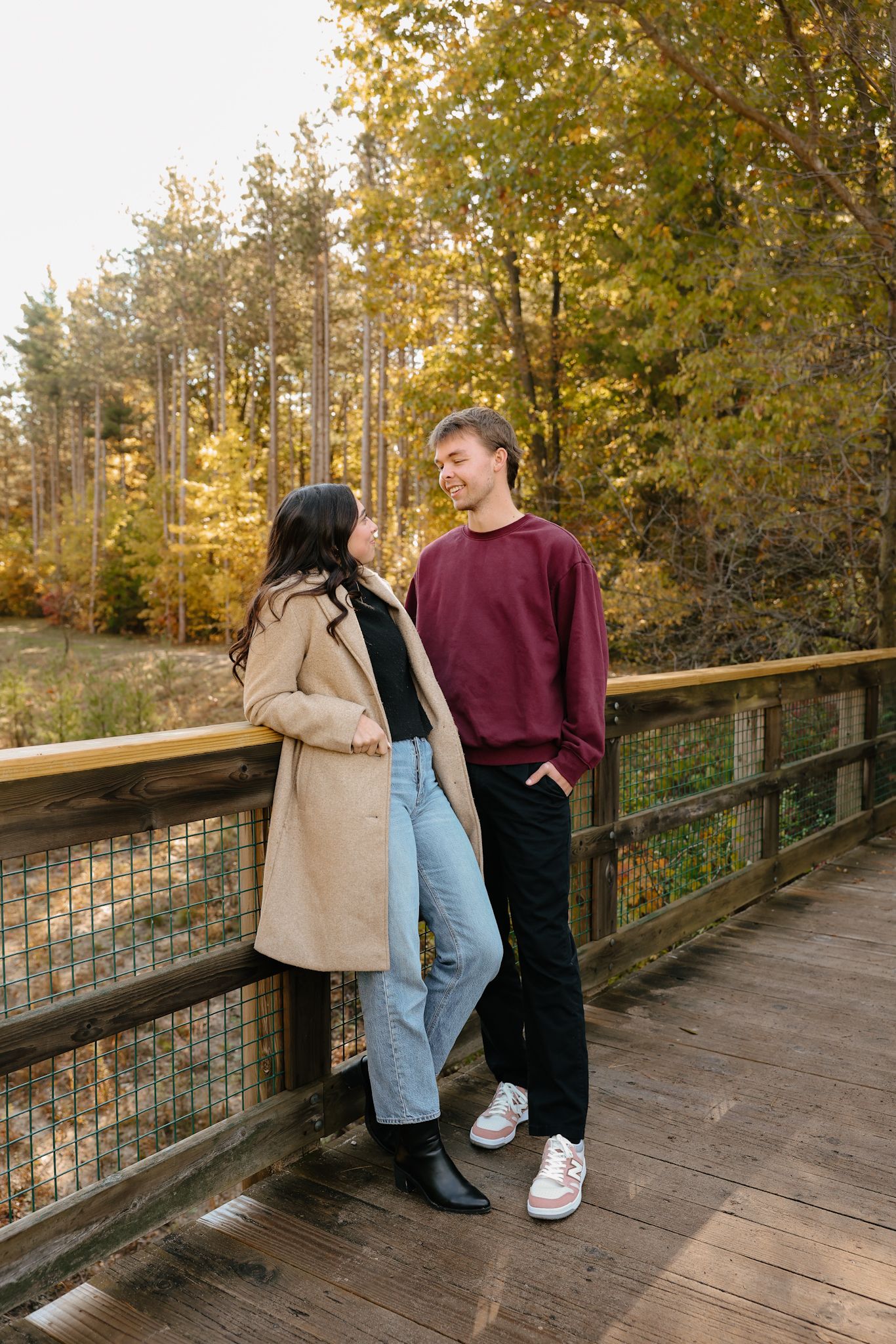 Couple in casual autumn outfits standing on wooden bridge during fall season.