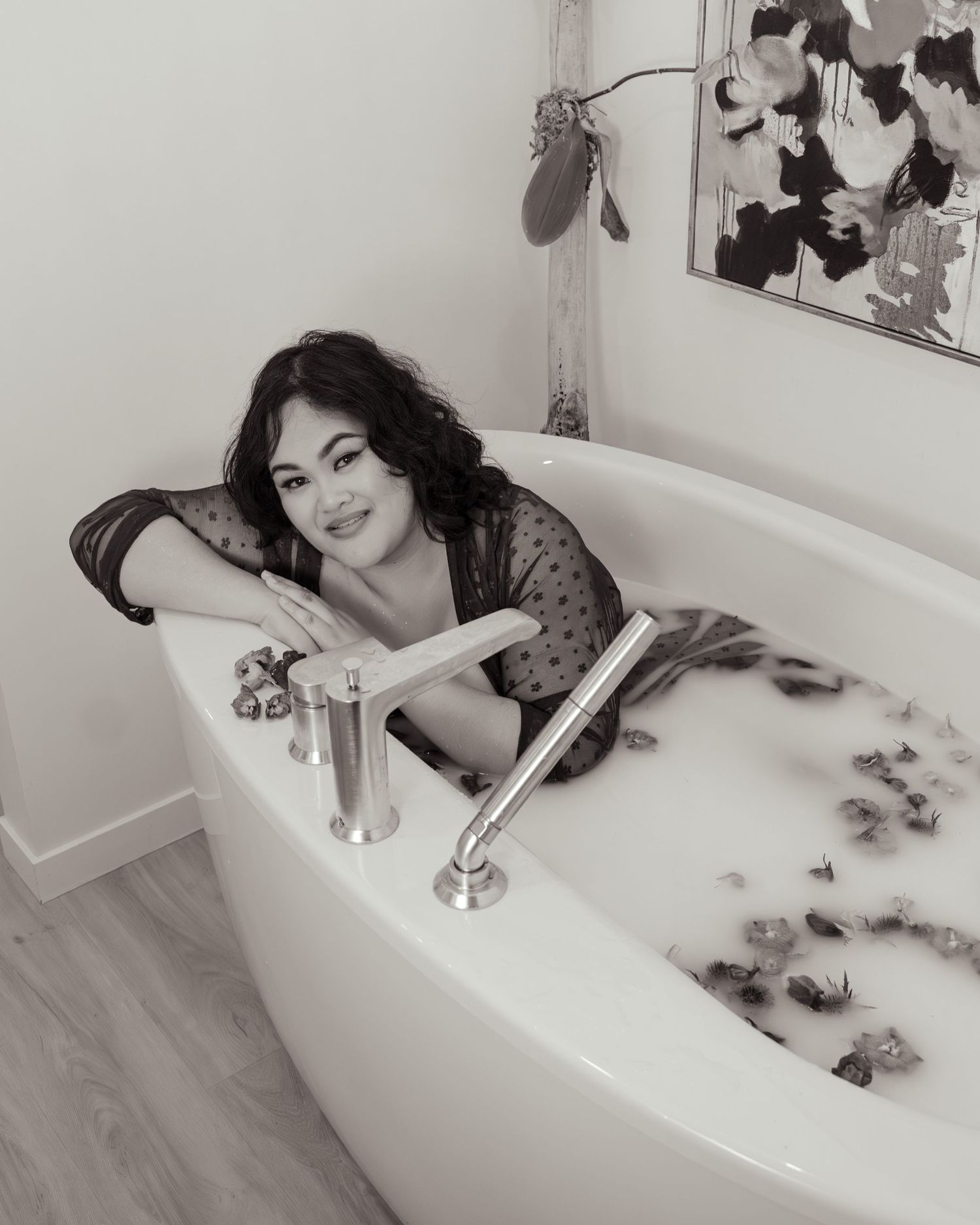 A person relaxes in a luxurious bubble bath with artistic photos displayed on the wall behind the bathtub.