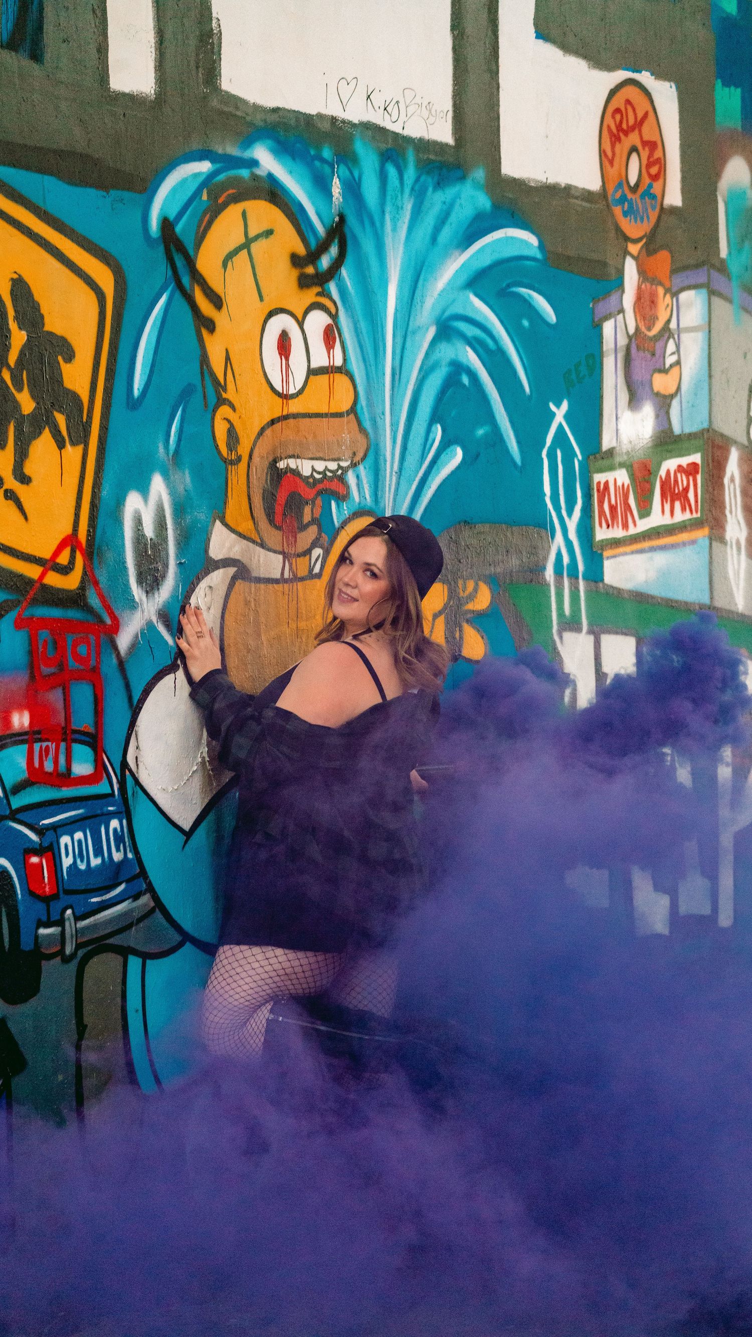 Urban photography with purple smoke bomb effect against cartoon street art mural.