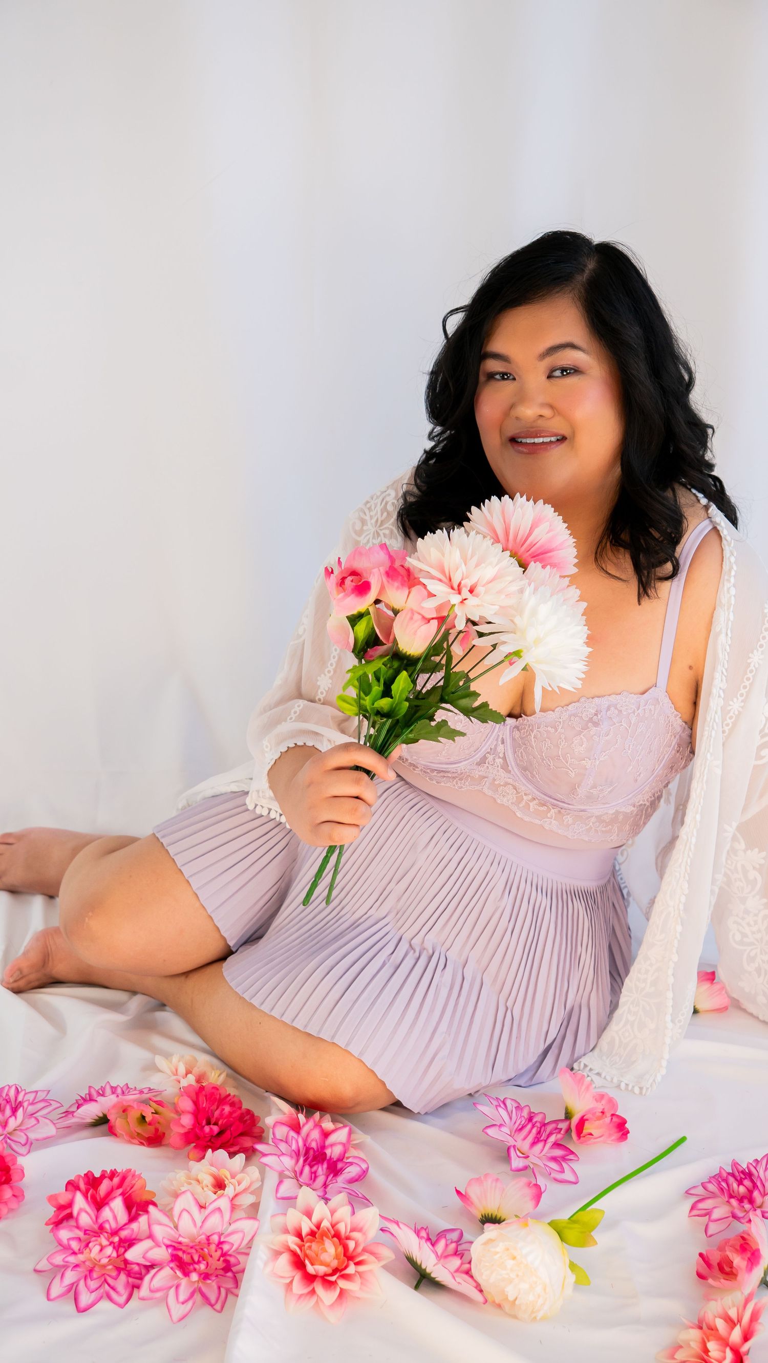 A feminine boudoir photo with pink flowers and white lace against a light background.
