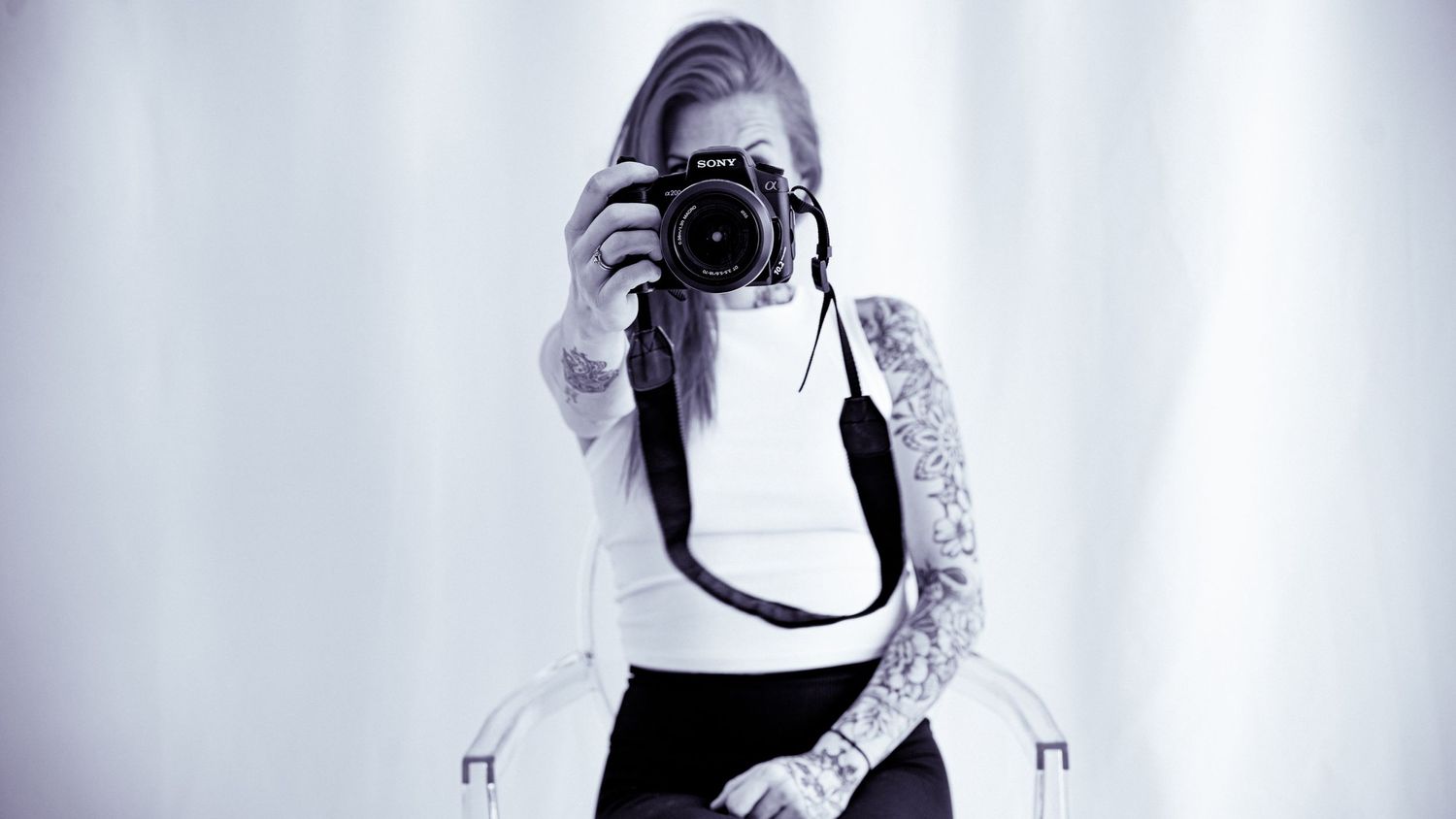 Photographer in black and white dress with tattoos takes a self portrait with a DSLR camera.