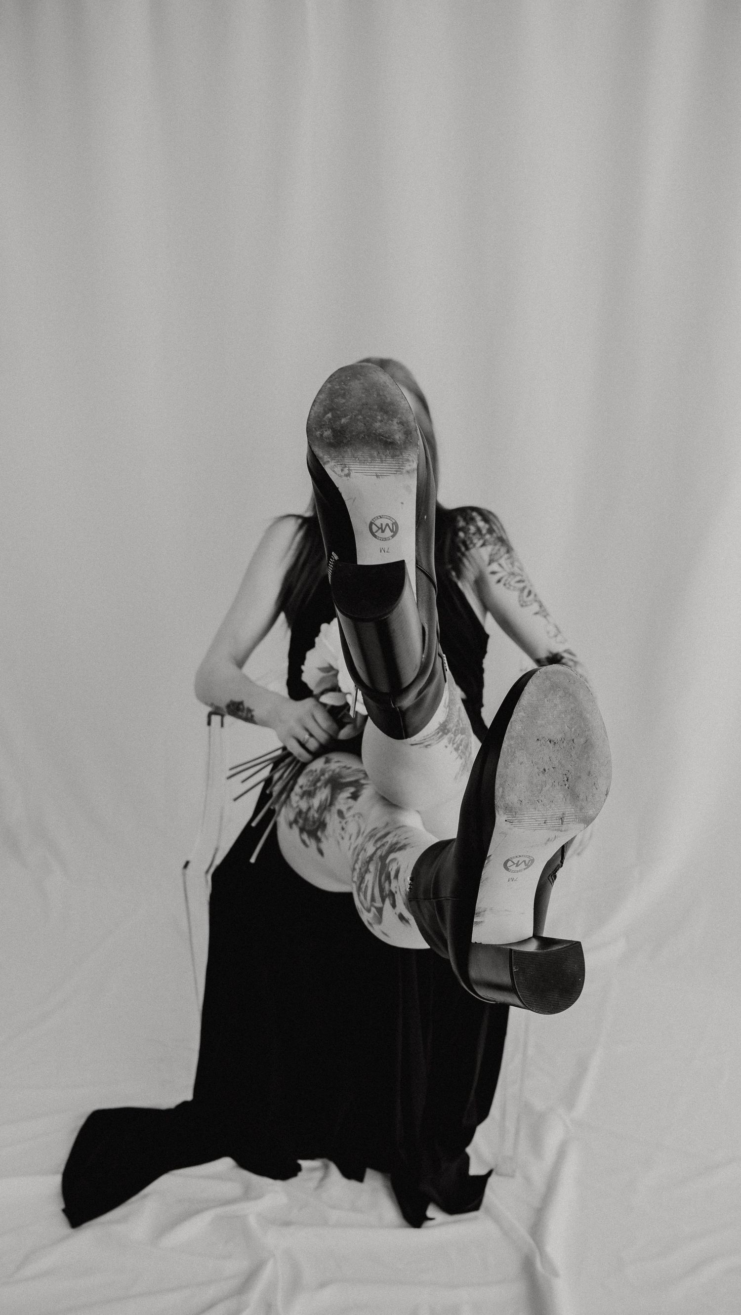 A black and white photo of a person in a black dress striking a dynamic dance pose against a light background.