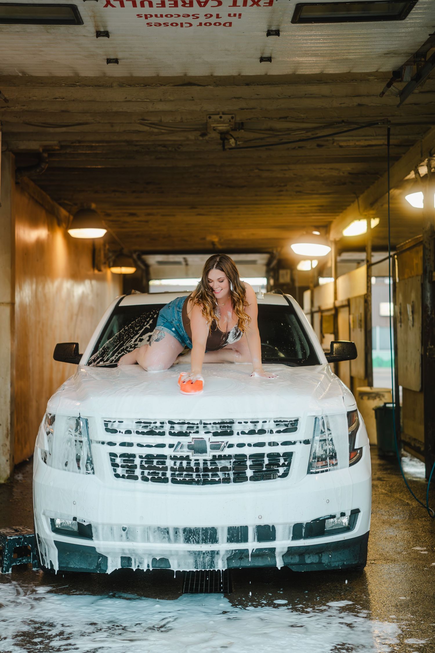A series of photos showing a white car being washed with soap and foam in a covered parking garage.
