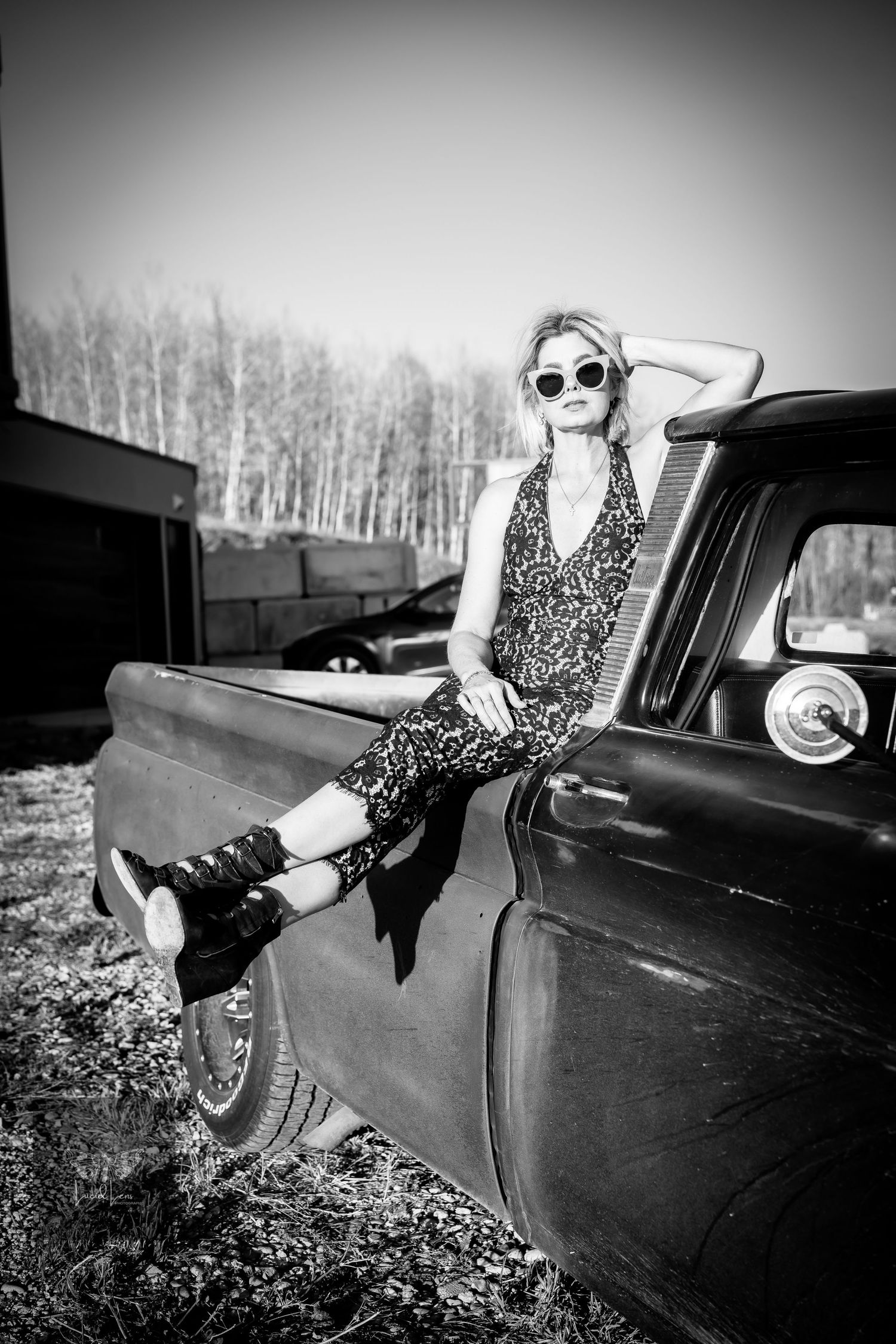A vintage black car is photographed with someone posing in polka dot dress and sunglasses in black and white.