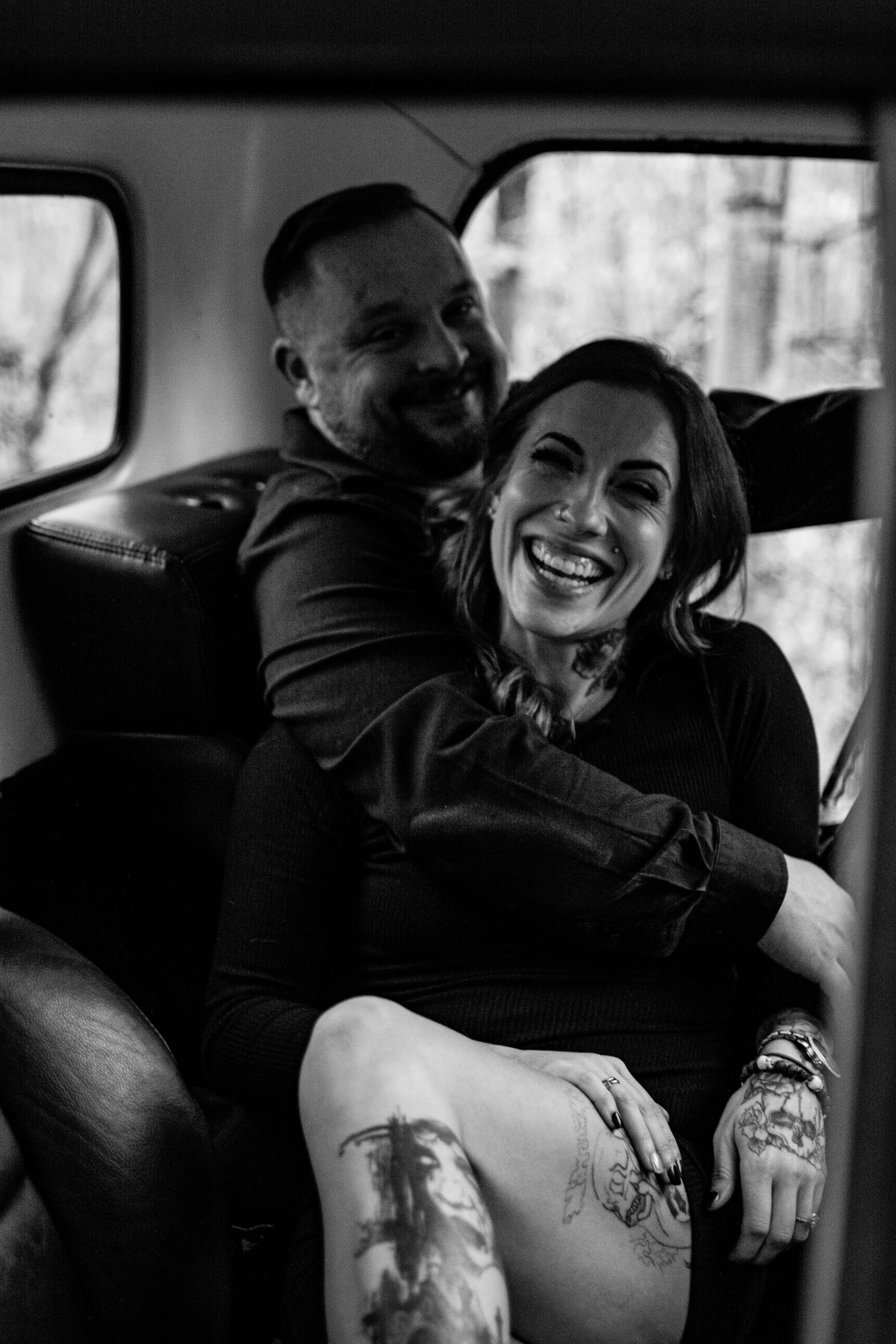 A black and white candid photo of a joyful couple laughing together in the backseat of a car.