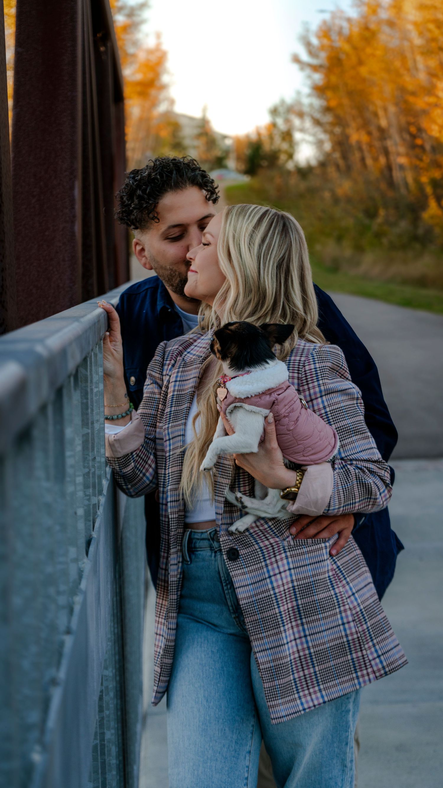 A romantic moment on a bridge with a small dog in a pink sweater during golden hour.