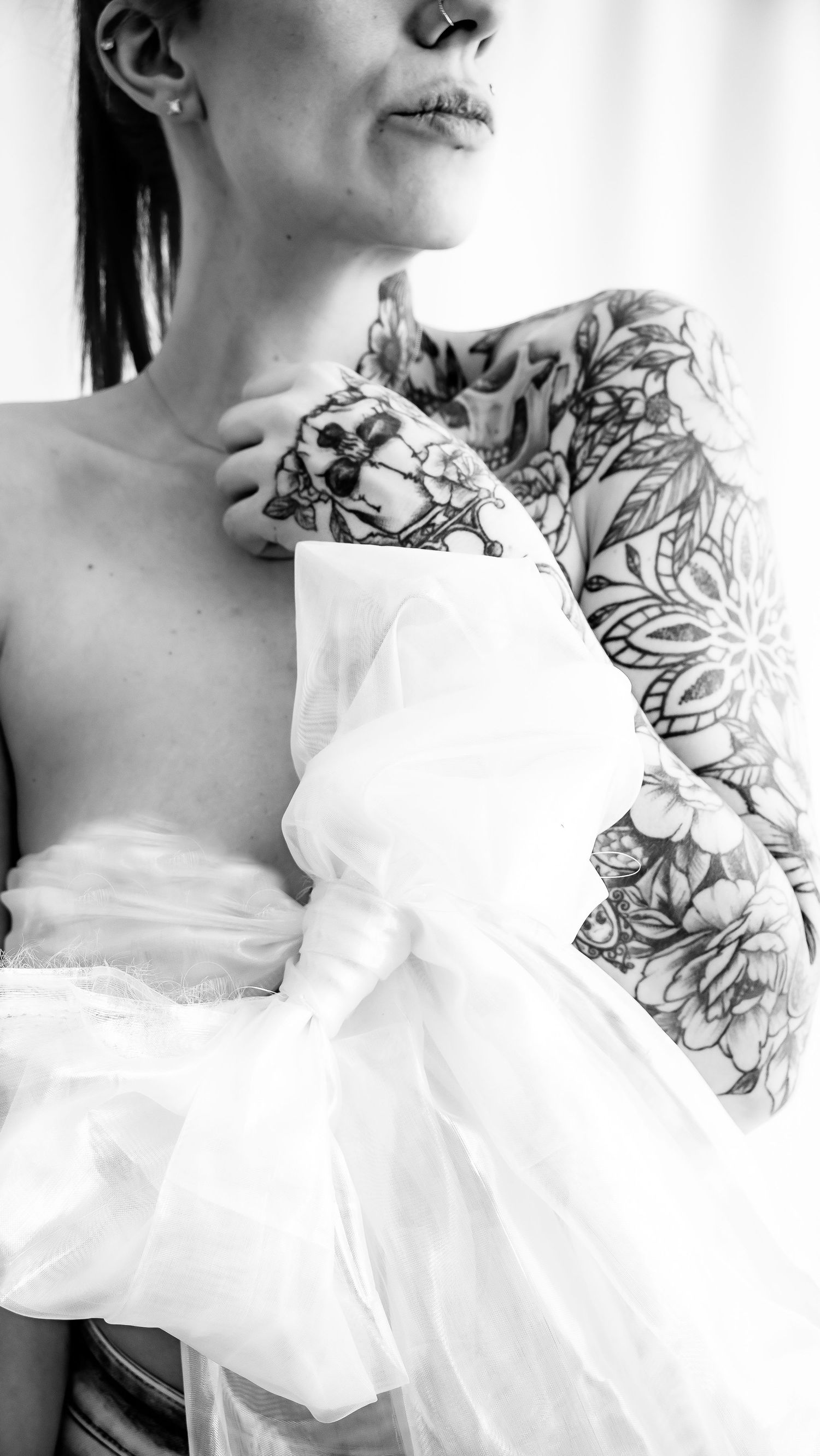 Black and white portrait showing intricate floral tattoo sleeve and flowing white fabric.