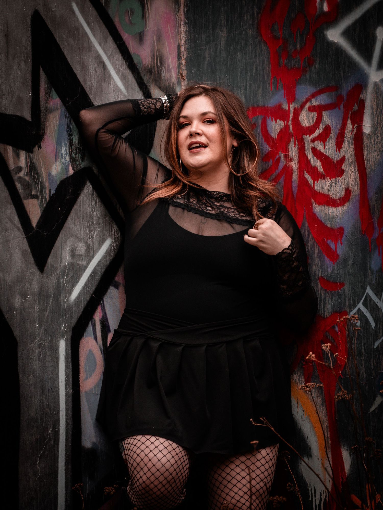 A model in a black dress poses dramatically against a graffiti wall with red accents in a moody photo series.