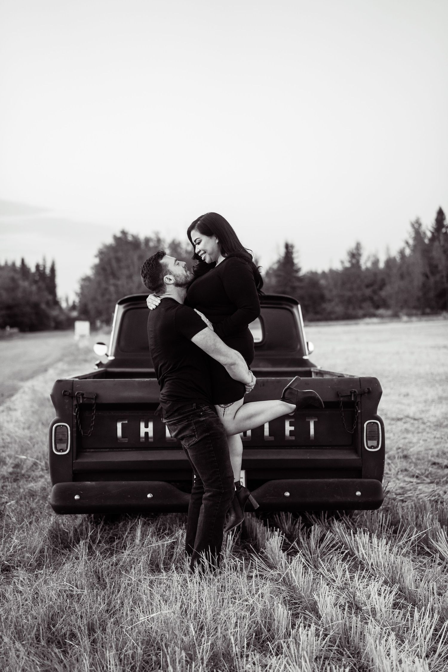 A romantic black and white photo series showing a couple embracing on the back of a vintage Chevrolet pickup truck in a field.
