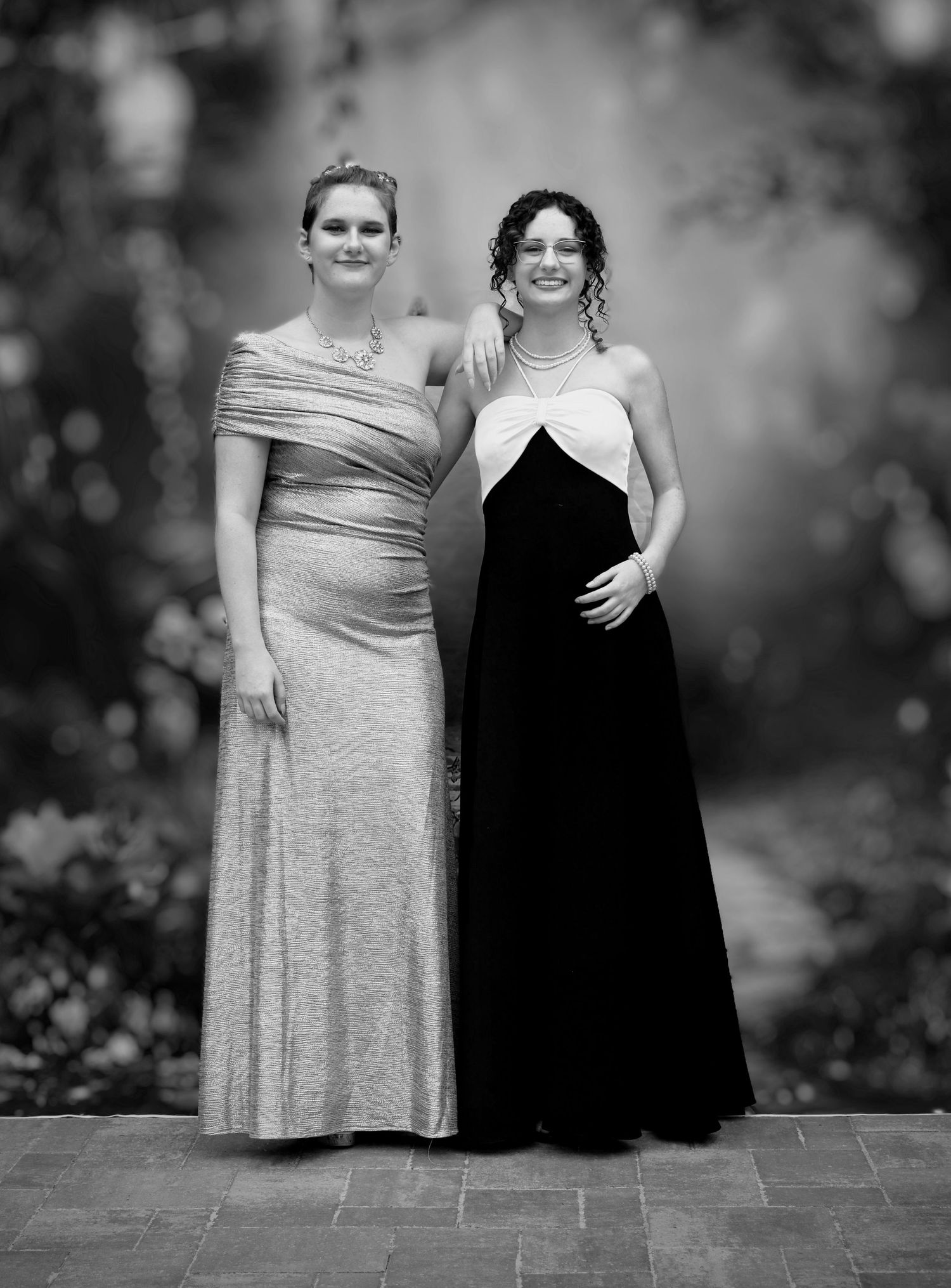 Posed B&W full-length portrait of sisters in prom dresses at Pace FL dinner event. Natural light, formal, fun, sisterly bond.