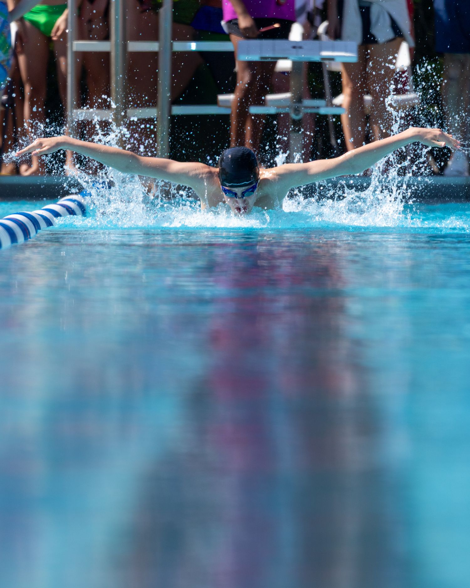 Competitive swimmer performing butterfly stroke in outdoor pool during swim meet, creating dramatic water splashes.