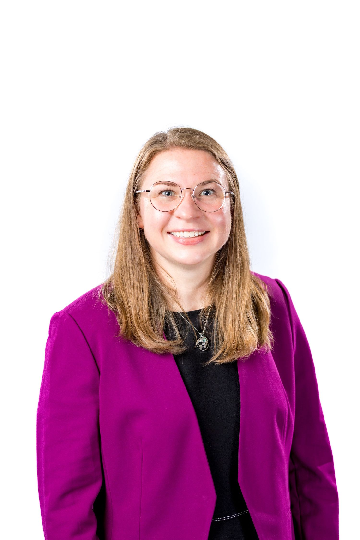 Smiling young woman with glasses and long hair wearing a purple blazer over a black top against white background.