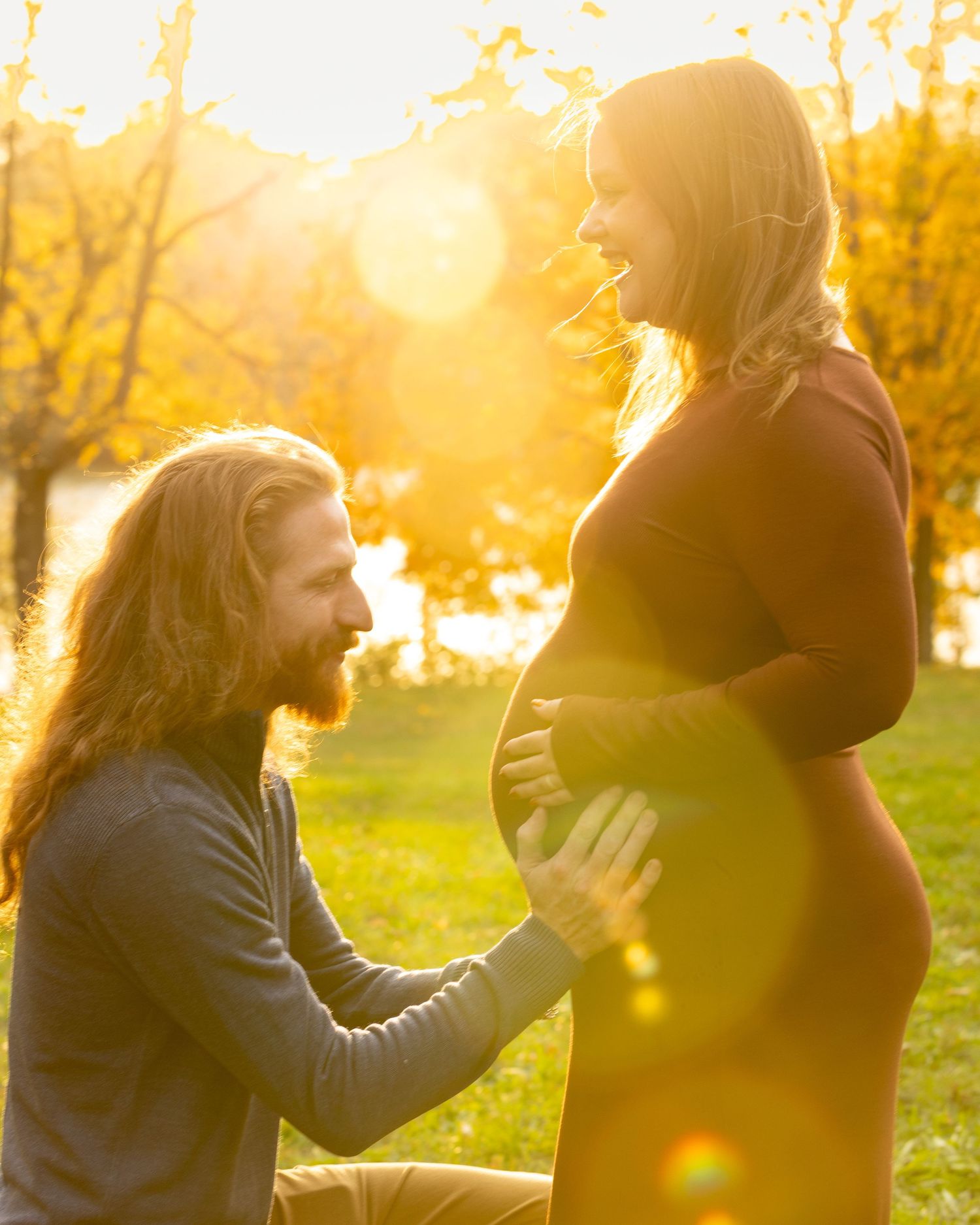 Silhouettes of people embracing in golden sunset light among autumn trees.