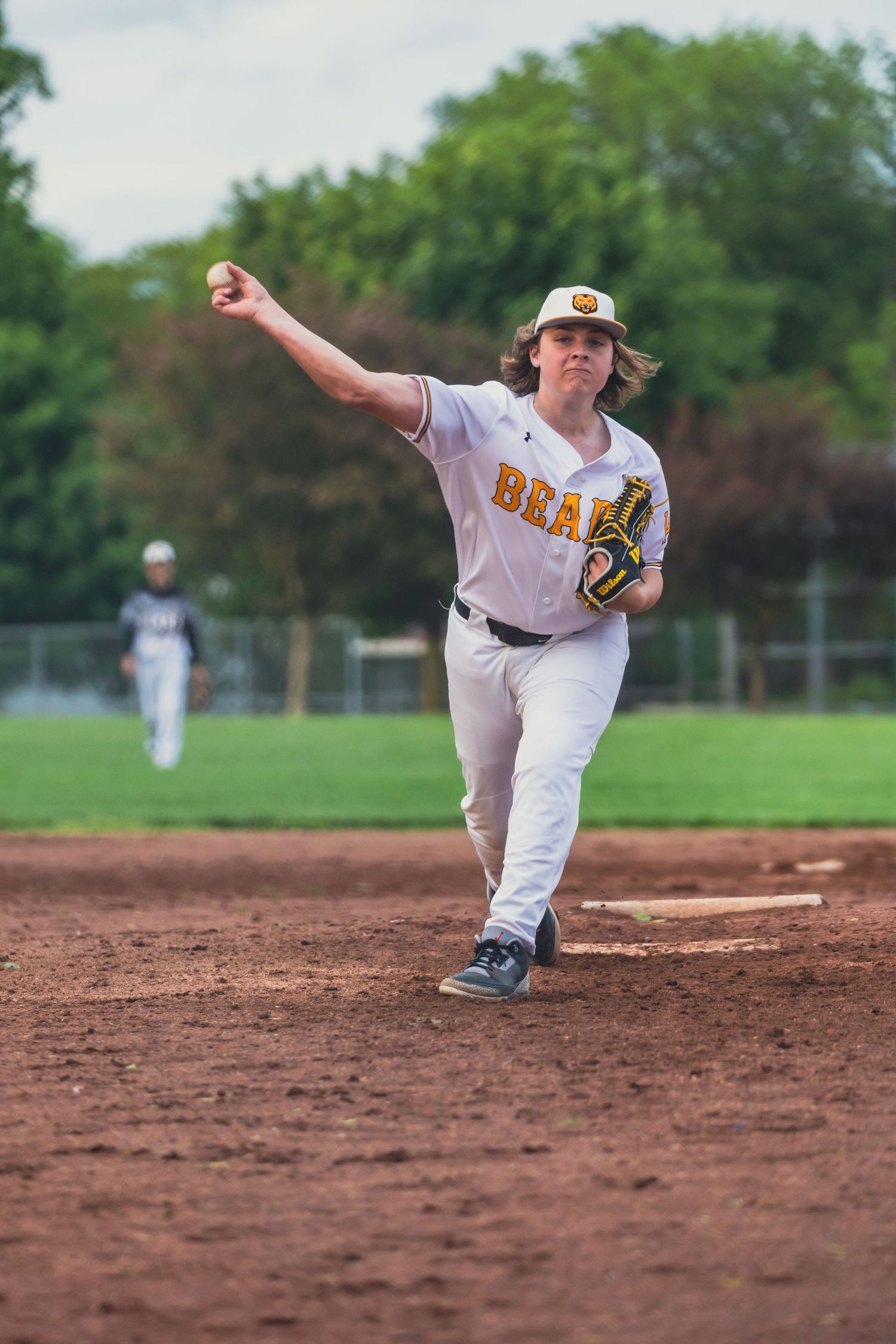 Young baseball pitcher in Bears uniform winds up to throw on a dirt infield during a youth league game.
