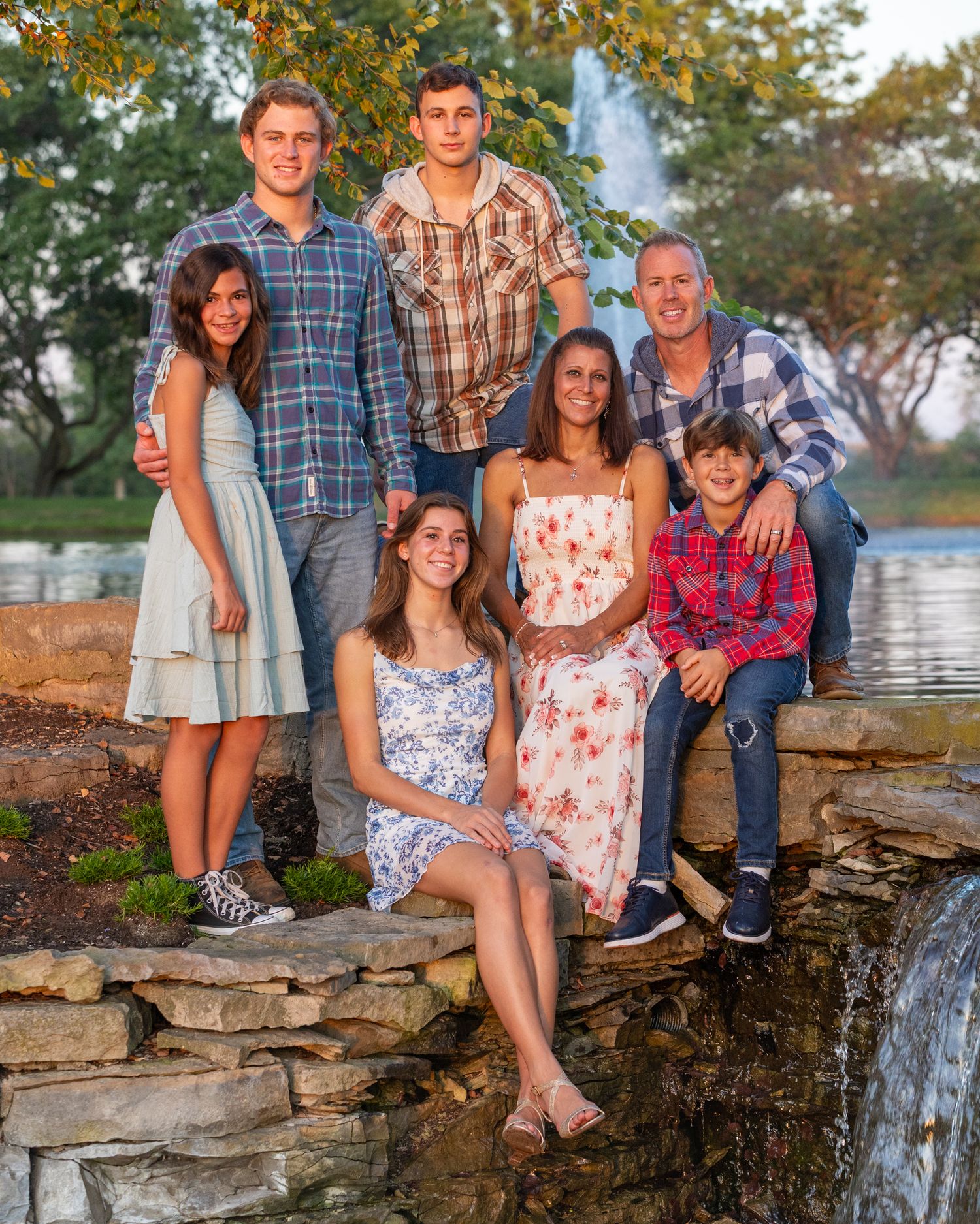 A family group poses together on a rocky ledge near water during an outdoor photo session at sunset.