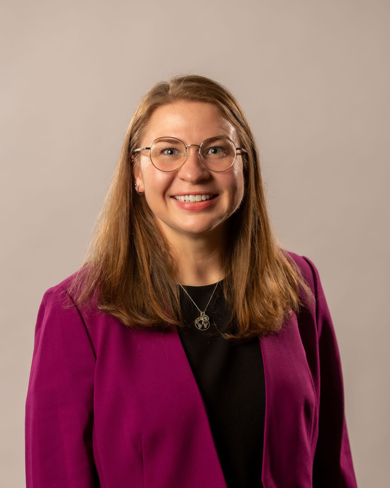Professional headshot of someone in a purple blazer and black top smiling warmly at the camera.