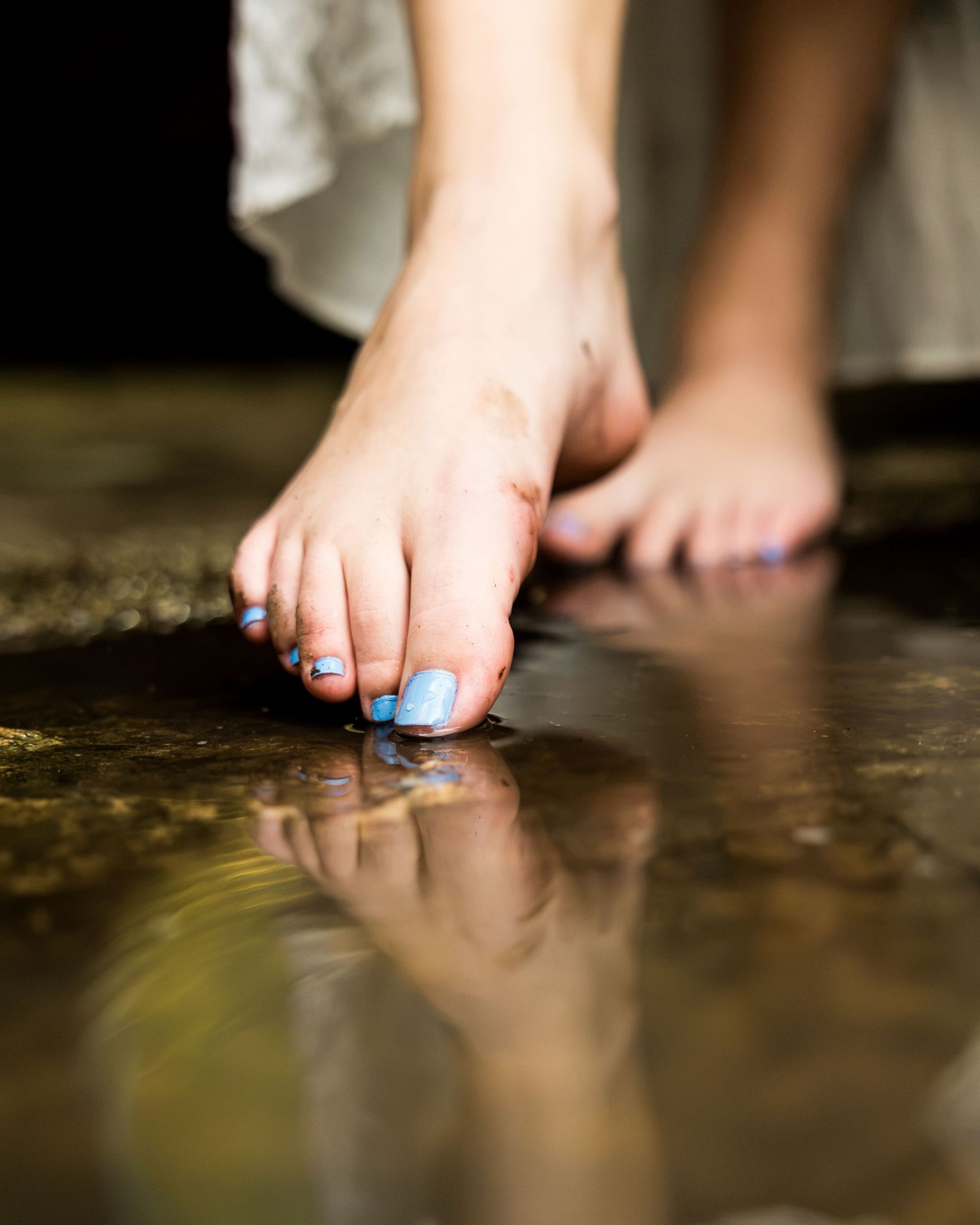 Close-up of bare feet with blue toenail polish touching a reflective water surface with ripples.