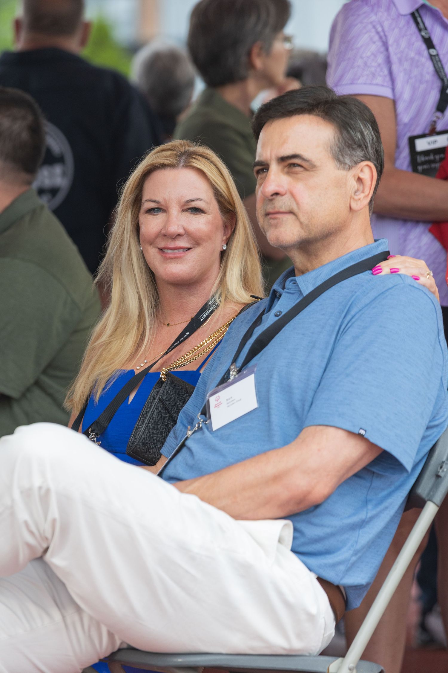 Smiling couple wearing lanyards sitting together at an outdoor event.