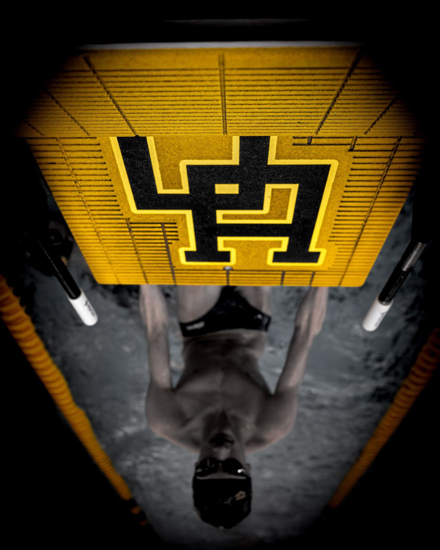 Artistic black and white security camera footage showing a figure walking beneath yellow numbered signs in a parking garage.