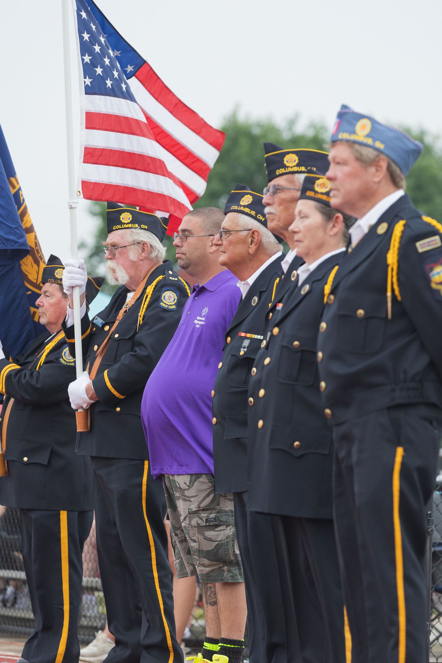 Veterans in uniform holding American flag during outdoor ceremony color guard.