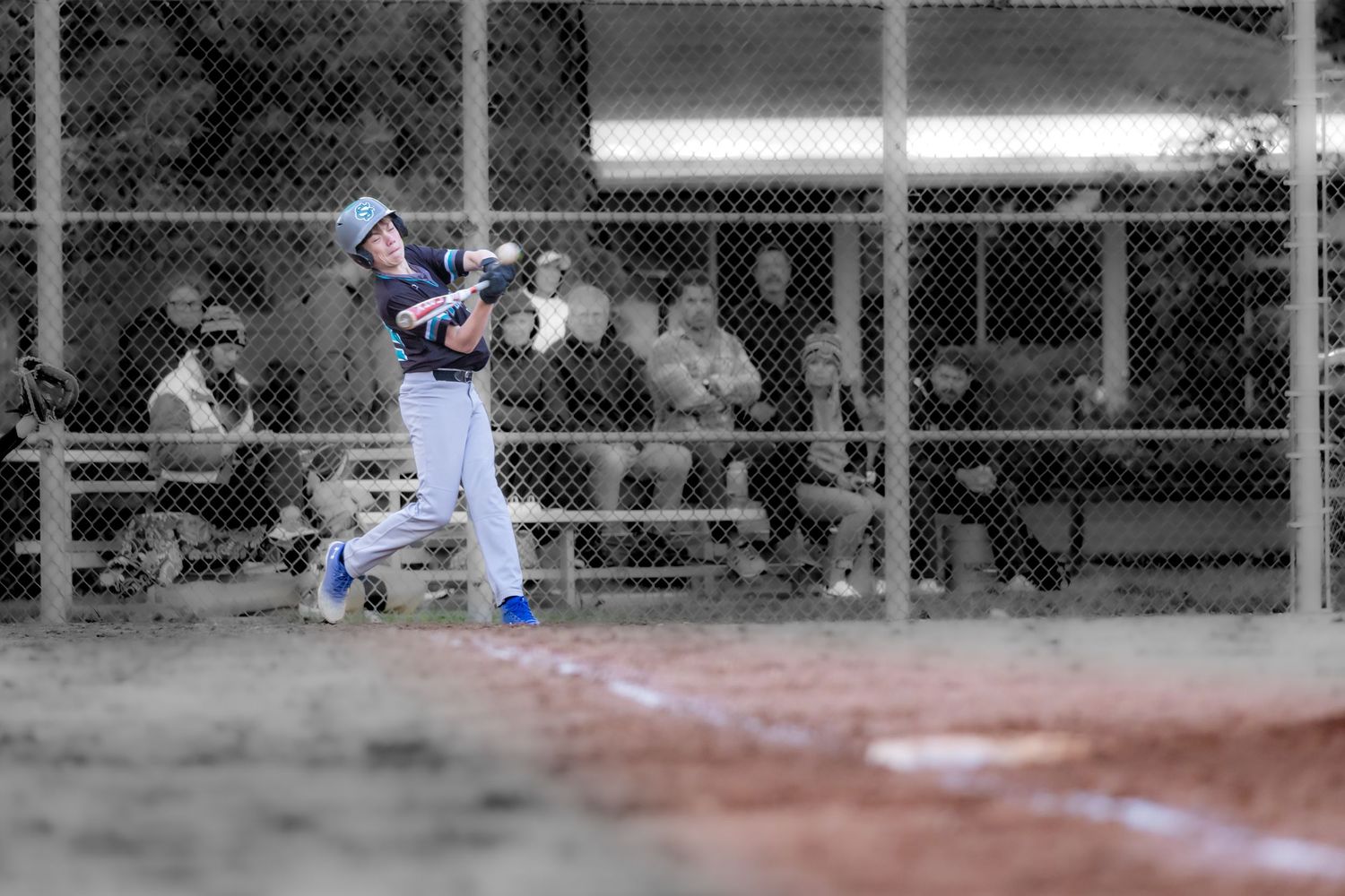 Youth baseball player swings bat during a game, wearing blue uniform at home plate.