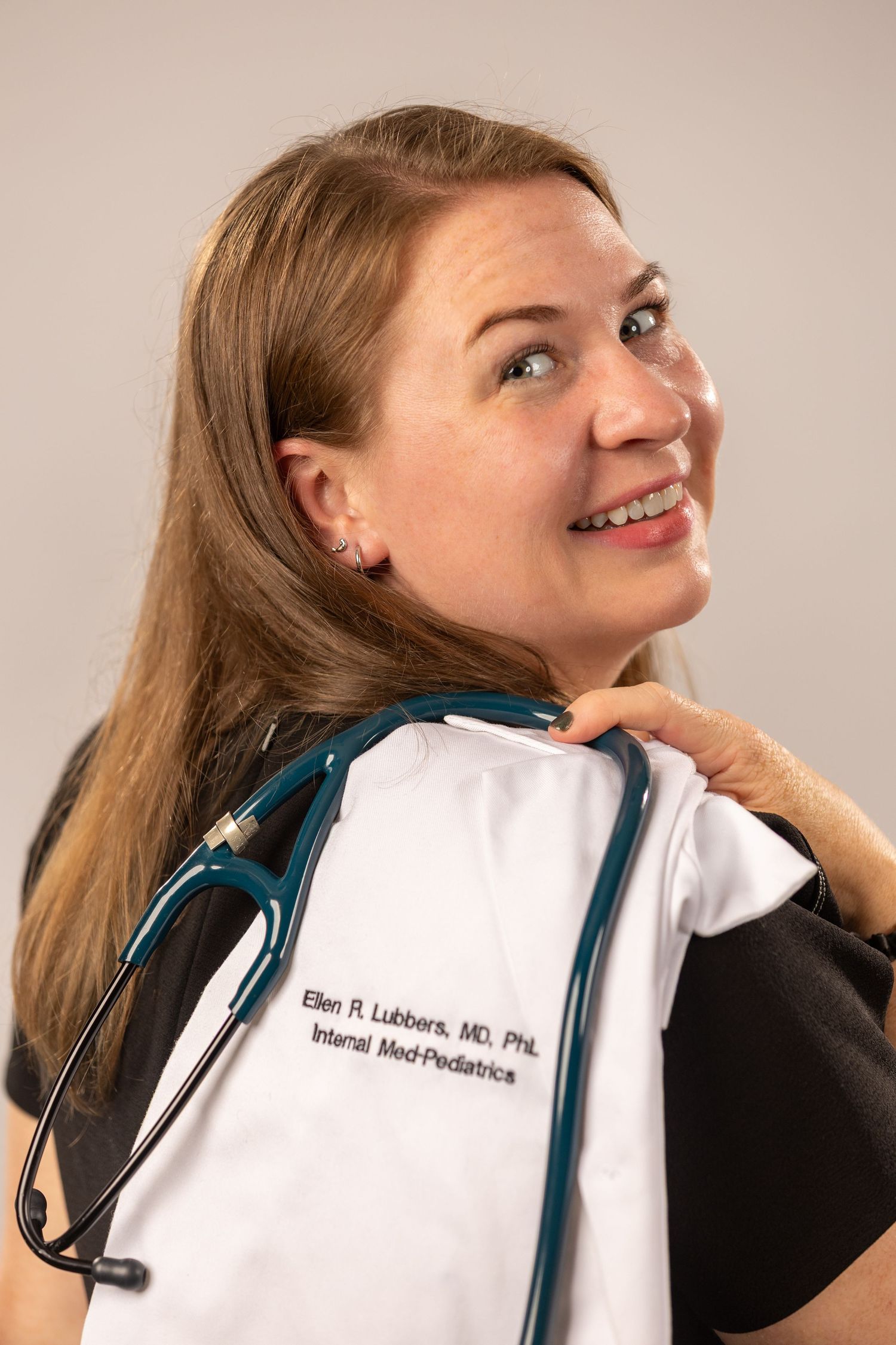 Medical professional in white coat shown in profile poses against neutral background.