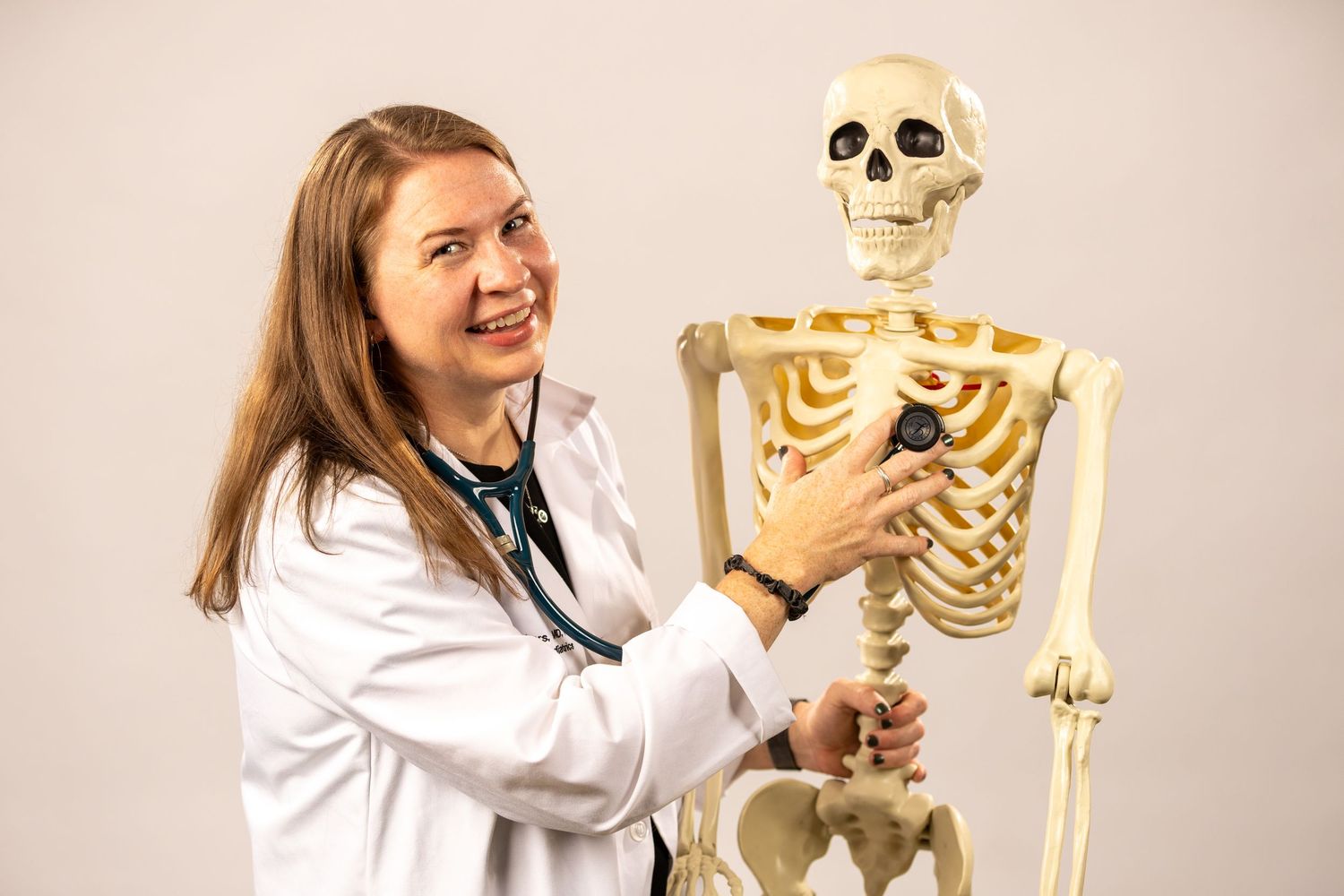 Healthcare provider in white coat interacting playfully with anatomical skeleton model.