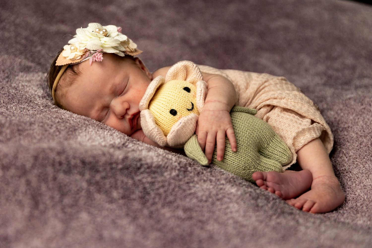 Sleeping newborn baby girl with floral headband cuddling a Winnie the Pooh stuffed animal on purple blanket.