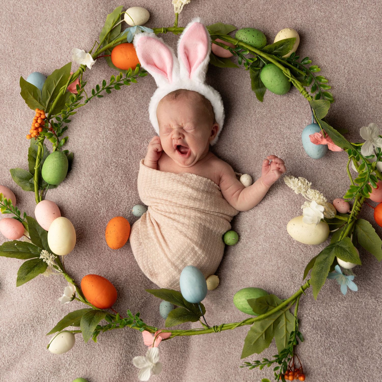 Baby styled with Easter decorations including eggs, flowers, and bunny ears on a neutral backdrop.