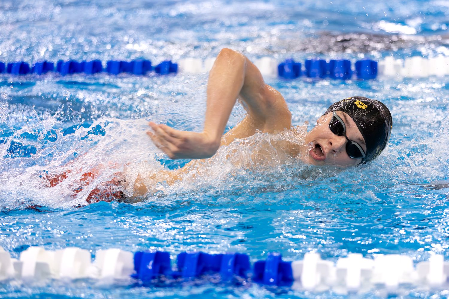 Competitive swimmer doing freestyle stroke in pool, wearing goggles and swim cap, splashing water during race.