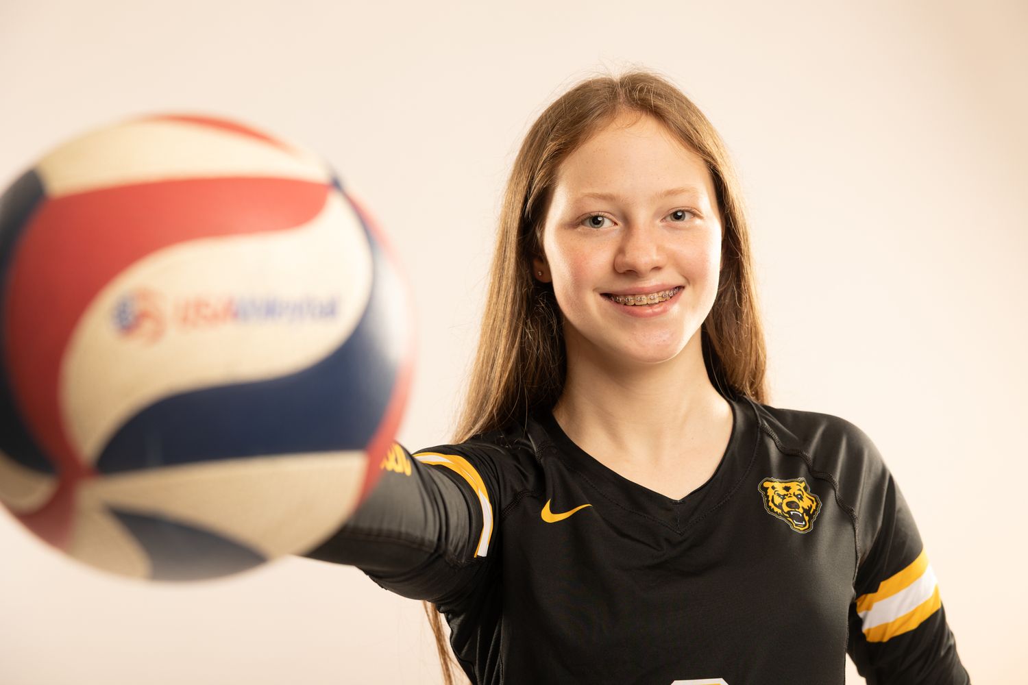 A volleyball player in a black uniform smiles while holding a red, white and blue volleyball.