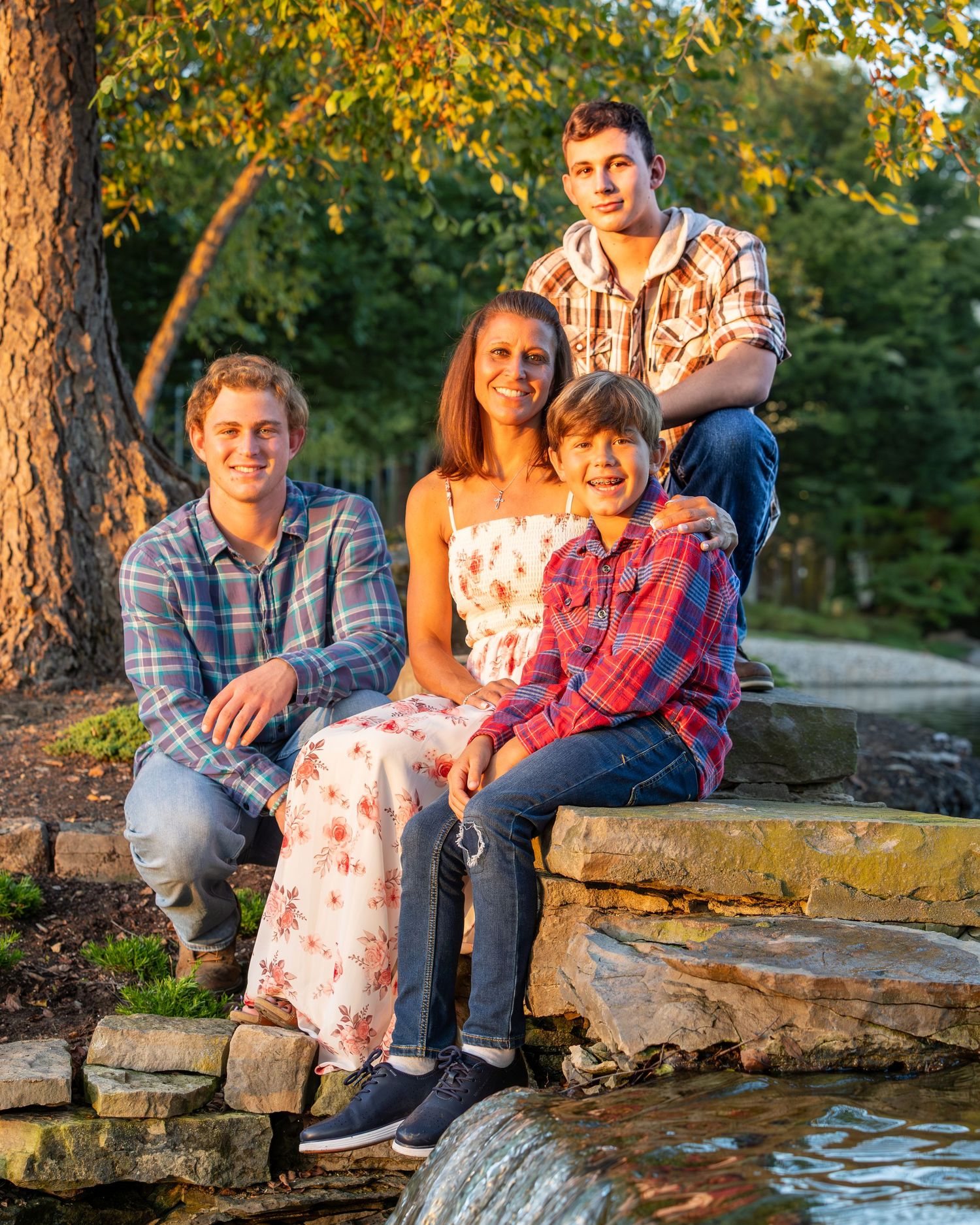 Family of four posing on stone steps near a pond surrounded by autumn trees in warm golden light.