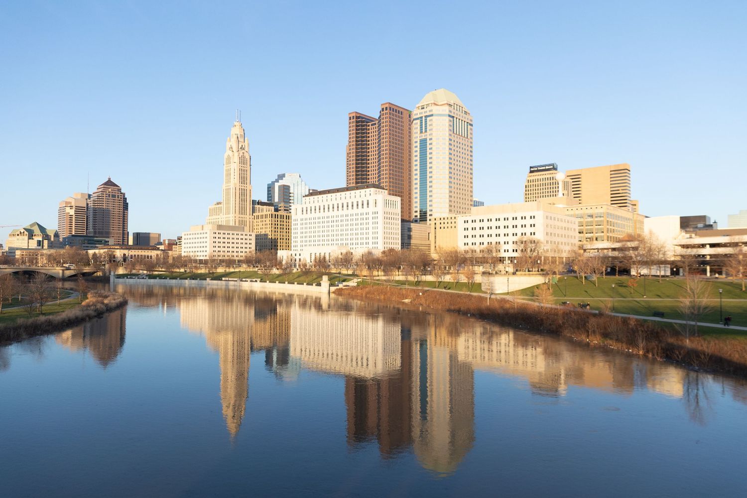 Columbus Ohio skyline reflecting in the Scioto River on a clear sunny day with modern skyscrapers.