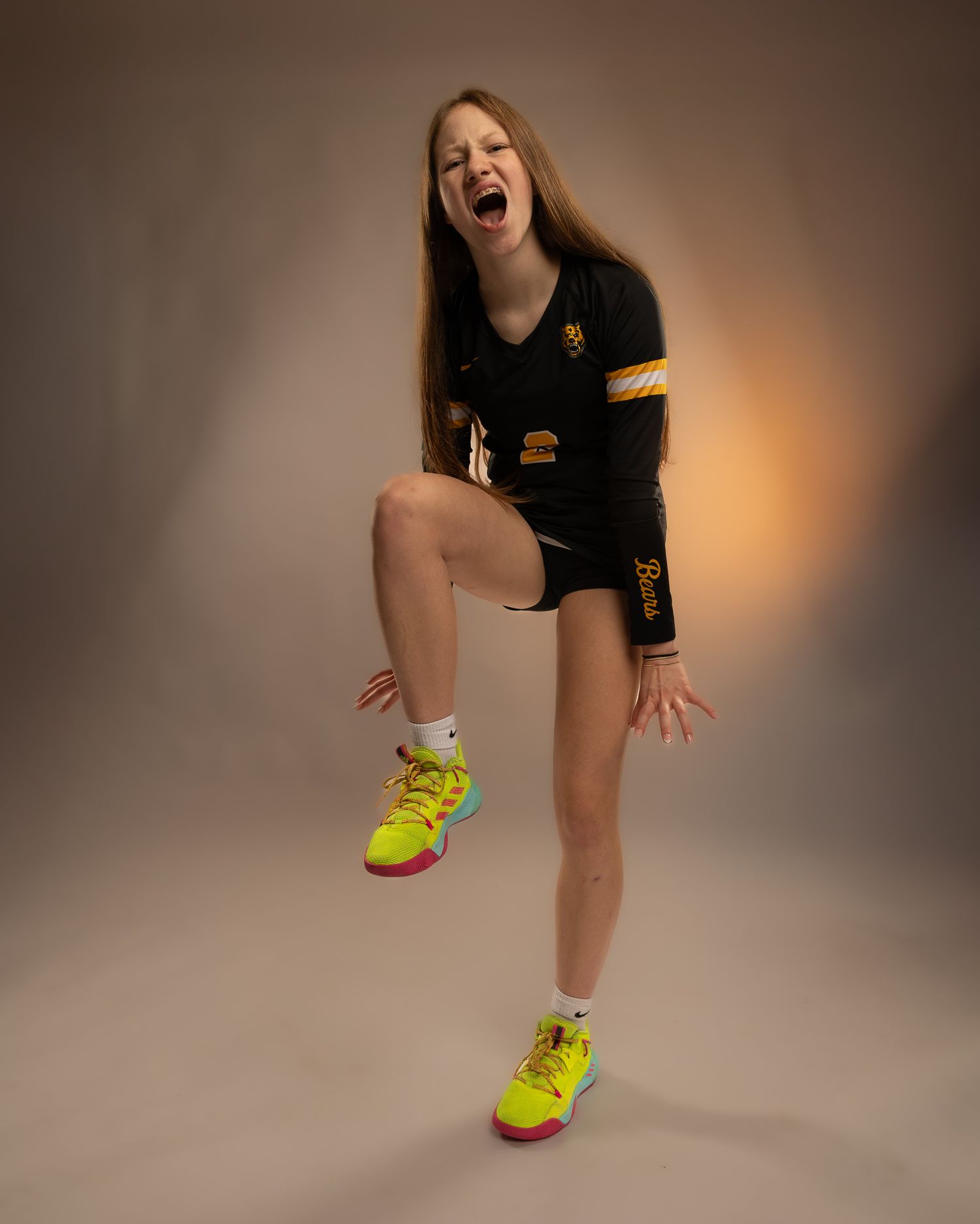 Energetic female volleyball player poses in black uniform with neon yellow shoes during photo shoot.