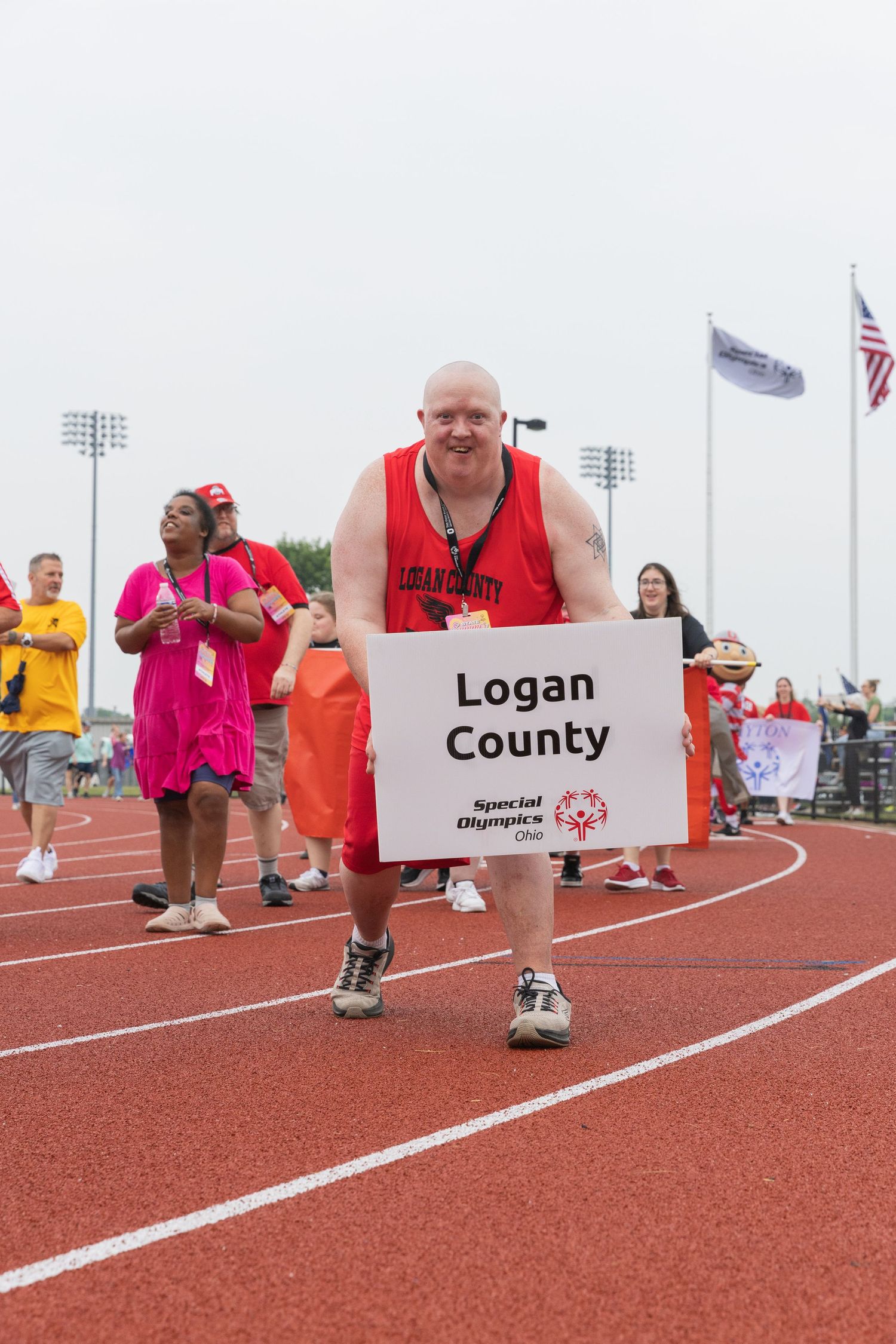 Man in red Logan County shirt carries Special Olympics Ohio sign on a track during an opening ceremony parade.