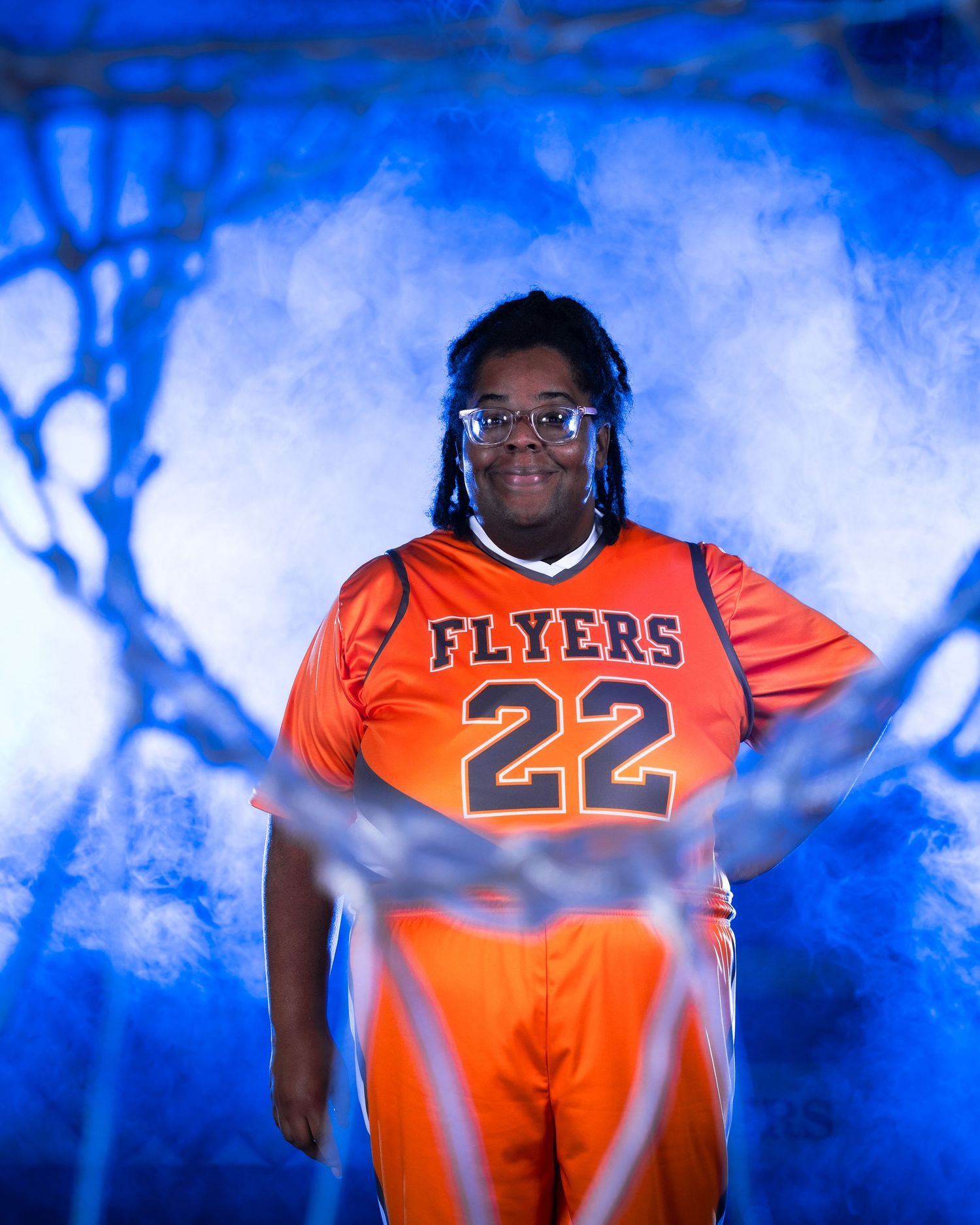 Player wearing orange Flyers jersey number 22 poses dramatically with blue smoke and basketball net backdrop.